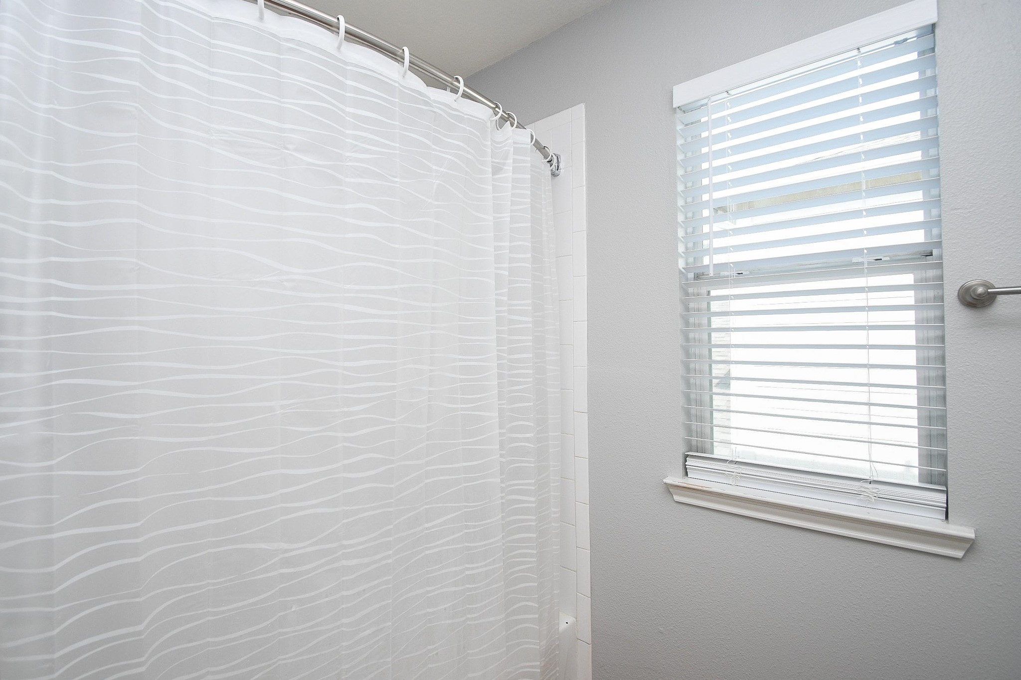 Bright bathroom featuring a modern shower with a textured curtain and a window for natural light.