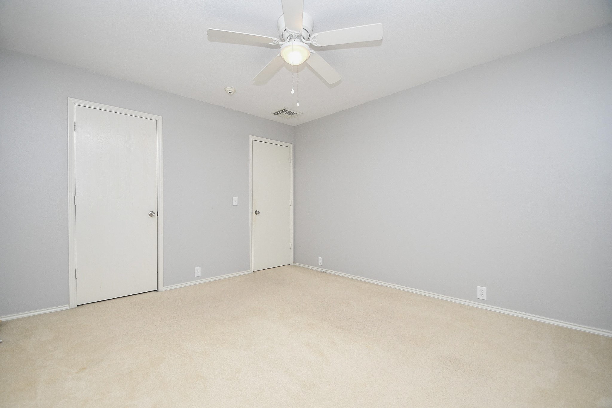 Bright and spacious room with neutral tones, featuring a ceiling fan and ample closet space for versatile use.