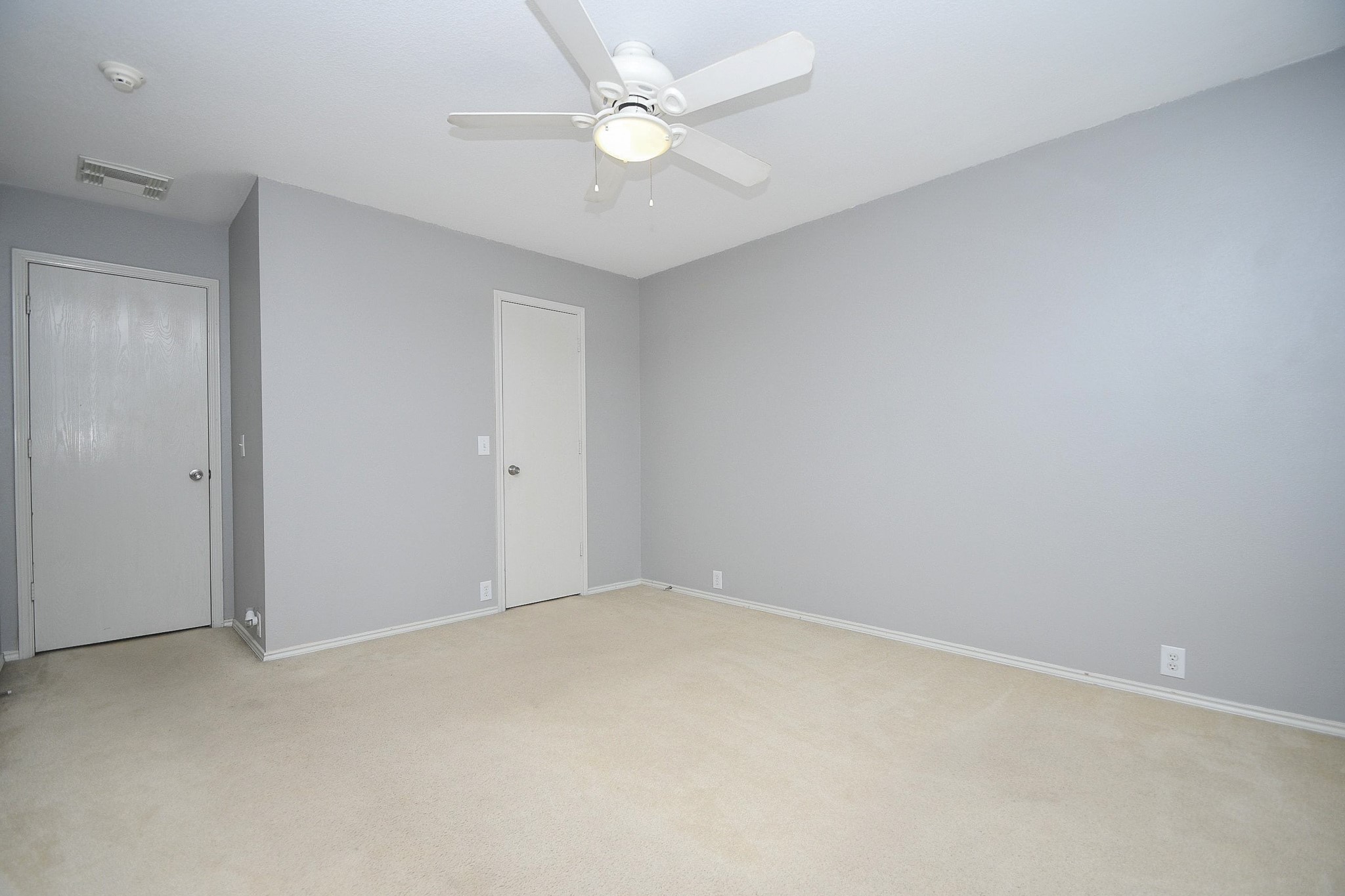 Spacious bedroom with neutral tones, featuring a ceiling fan and plush carpeting, offering a serene and comfortable atmosphere.