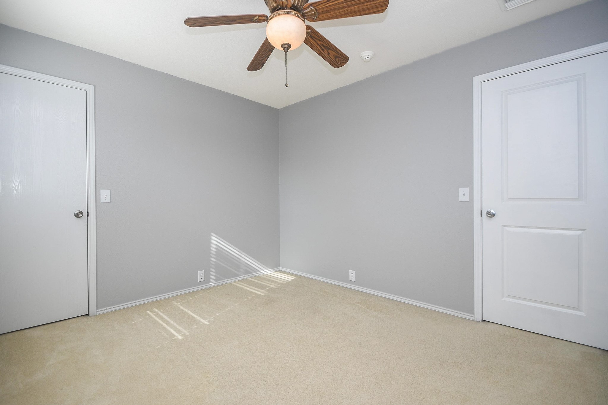 Bright, neutral-toned bedroom featuring a ceiling fan, soft carpeting, and ample natural light from a side window.