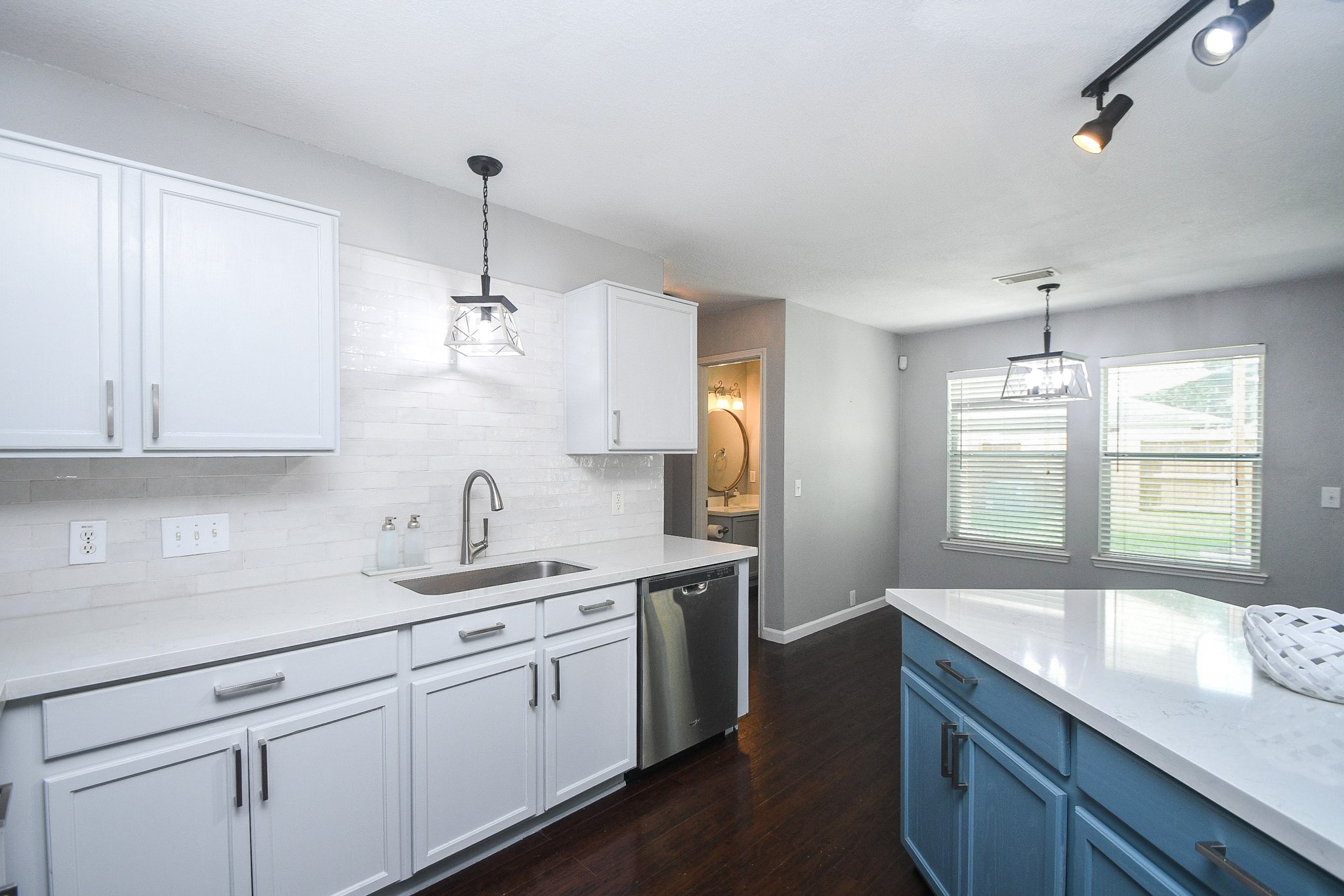 Bright kitchen featuring modern white cabinetry, sleek stainless steel appliances, and a stylish island with blue accents, complemented by dark hardwood floors and ample natural light.