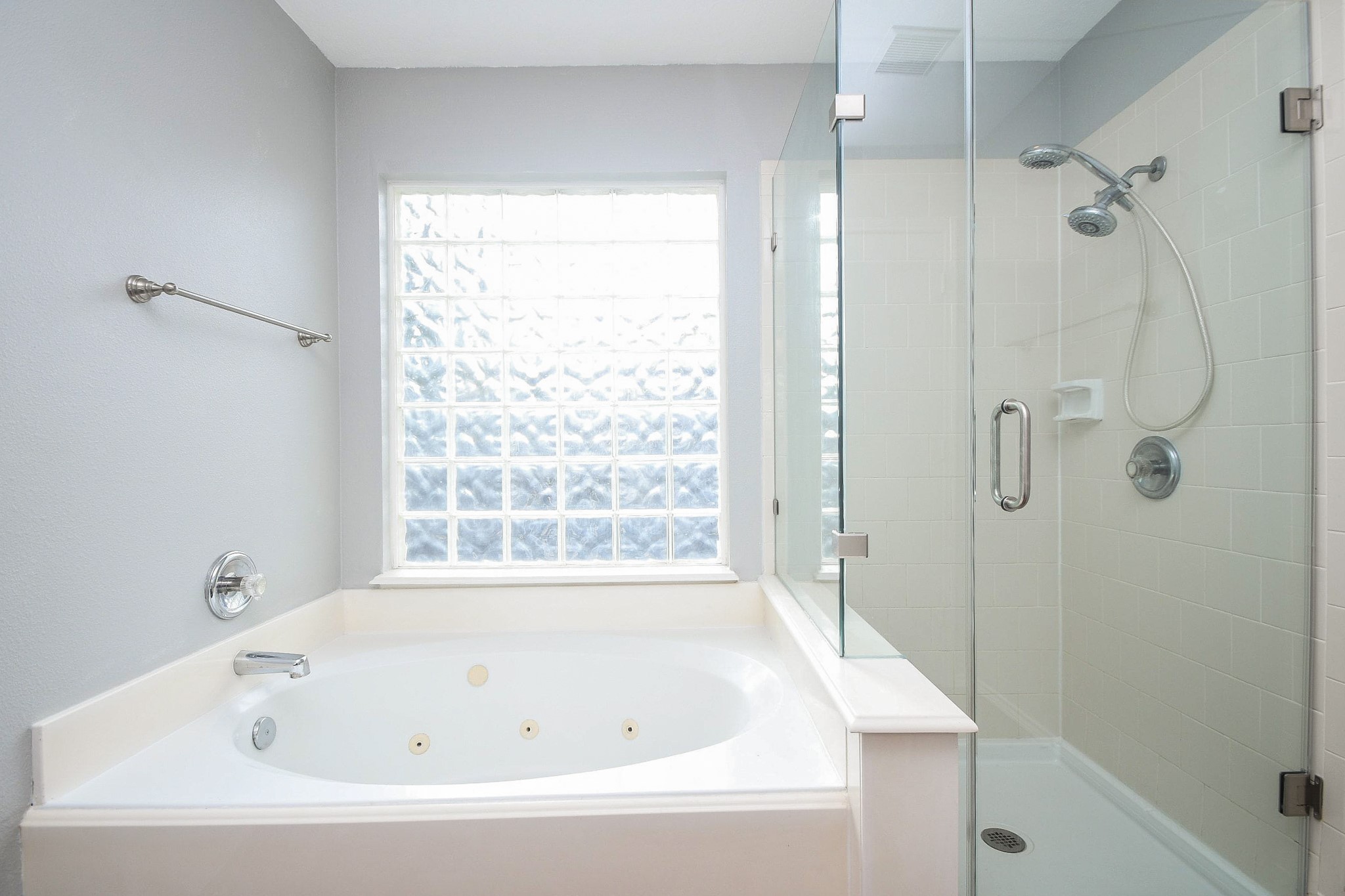 Bright bathroom featuring a luxurious jetted tub and a sleek glass-enclosed shower, complemented by a large frosted window for natural light and privacy.
