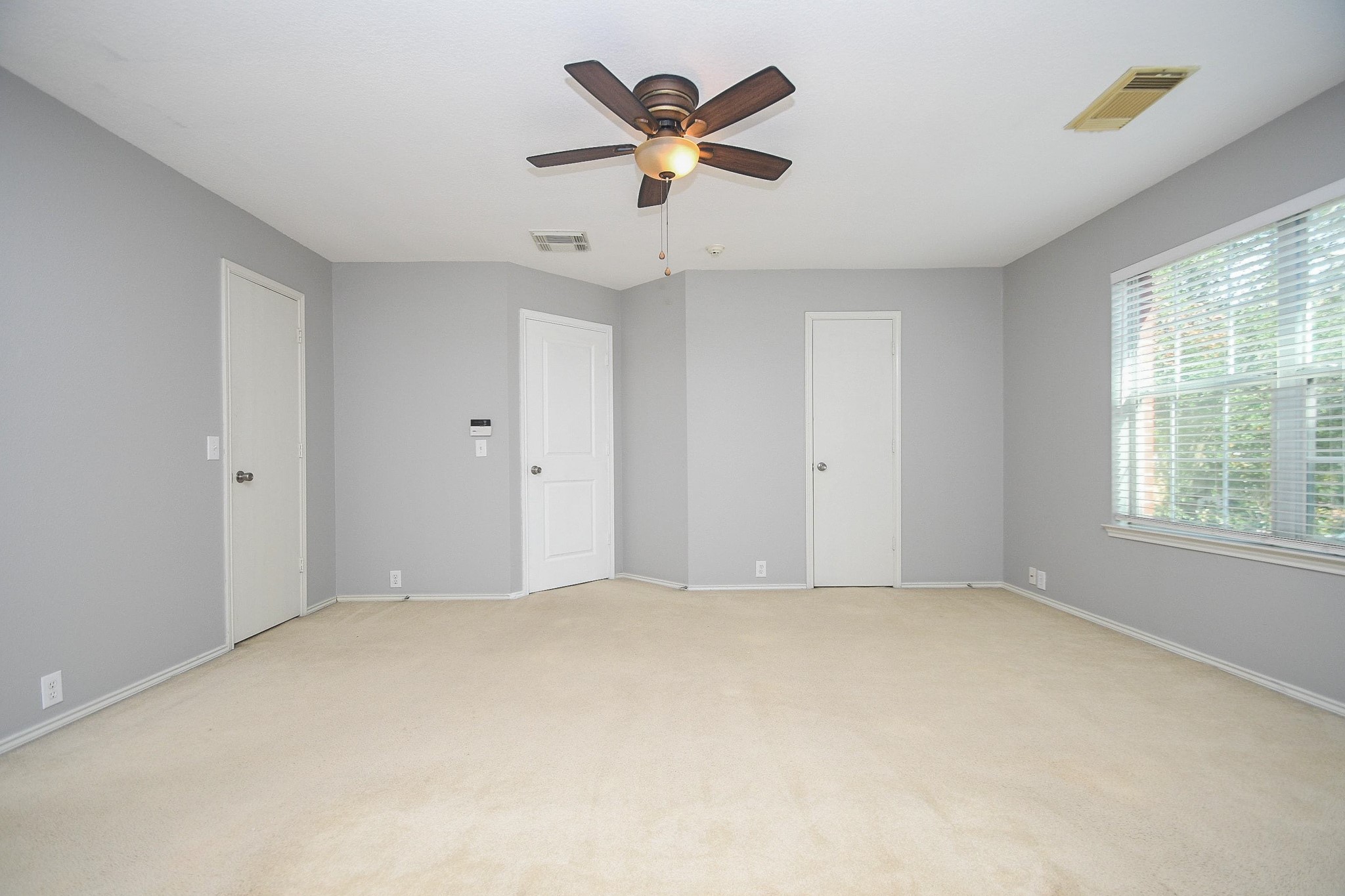 Spacious bedroom with soft carpet, neutral walls, a ceiling fan, and abundant natural light from a large window.
