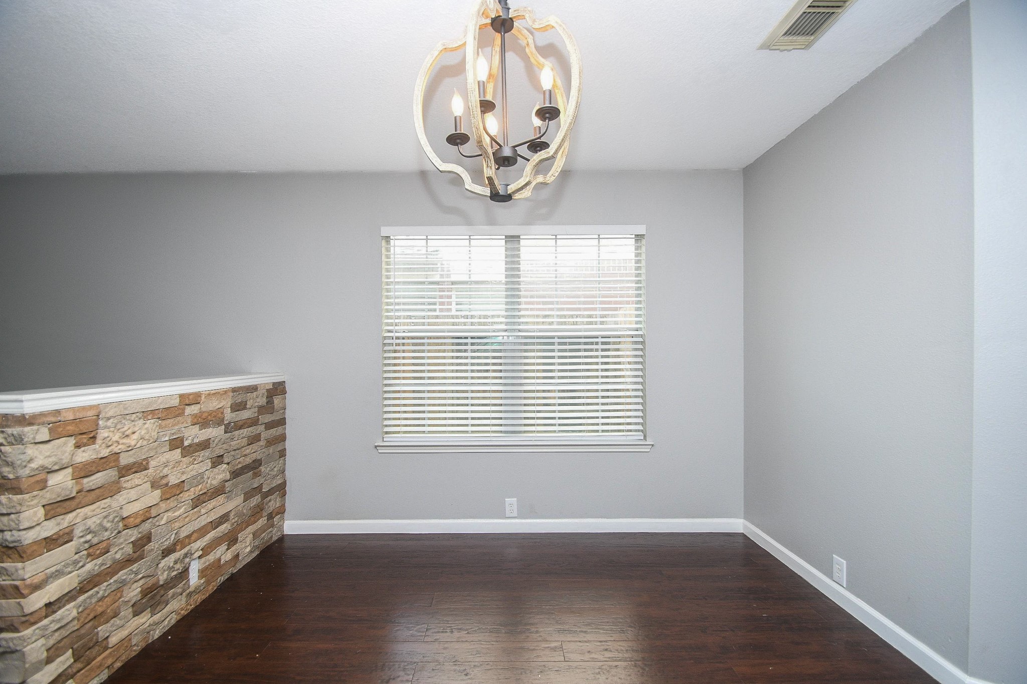 Charming room featuring a modern chandelier, rich dark wood flooring, and a stylish stone accent wall, creating an inviting atmosphere.
