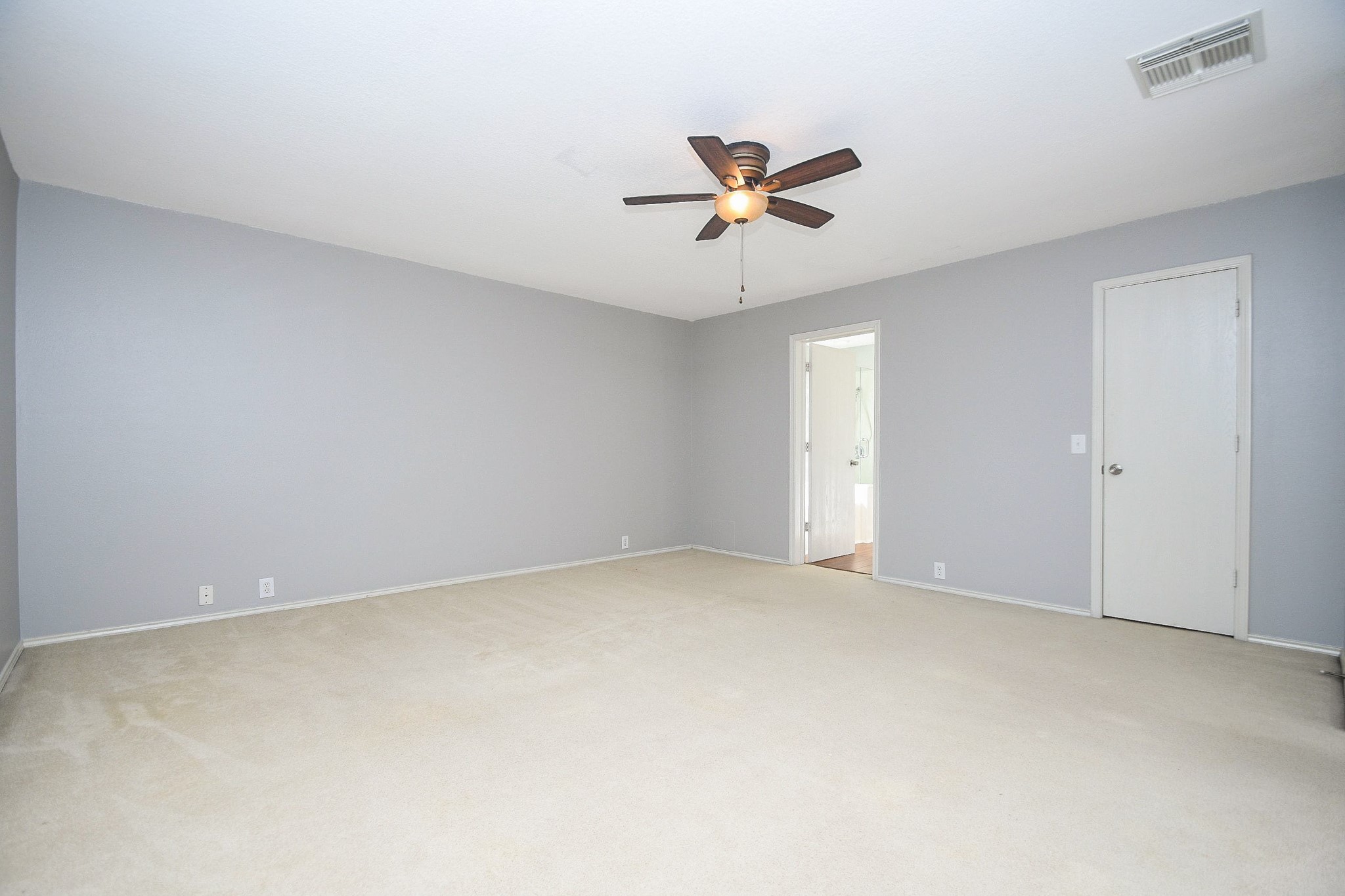 Spacious bedroom with neutral carpeting, soft gray walls, and a ceiling fan, offering a welcoming atmosphere and ample natural light.