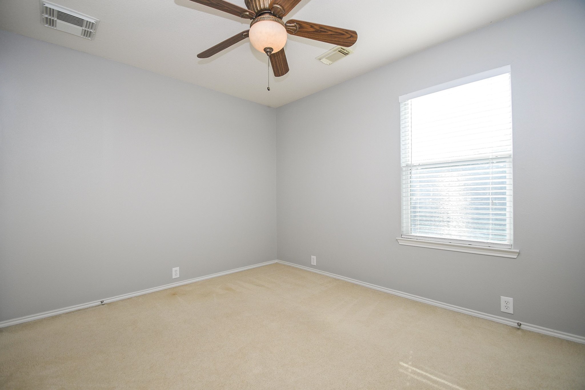 Bright and inviting room with soft gray walls, a large window for natural light, and a ceiling fan for comfort.