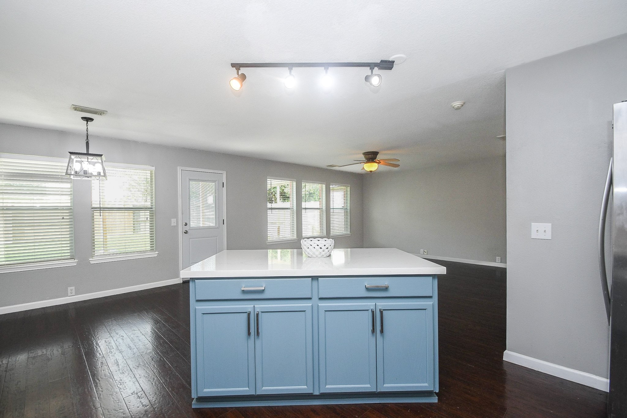 Spacious open-concept living area featuring a modern kitchen island with a stylish blue base, ample natural light, and sleek hardwood floors.