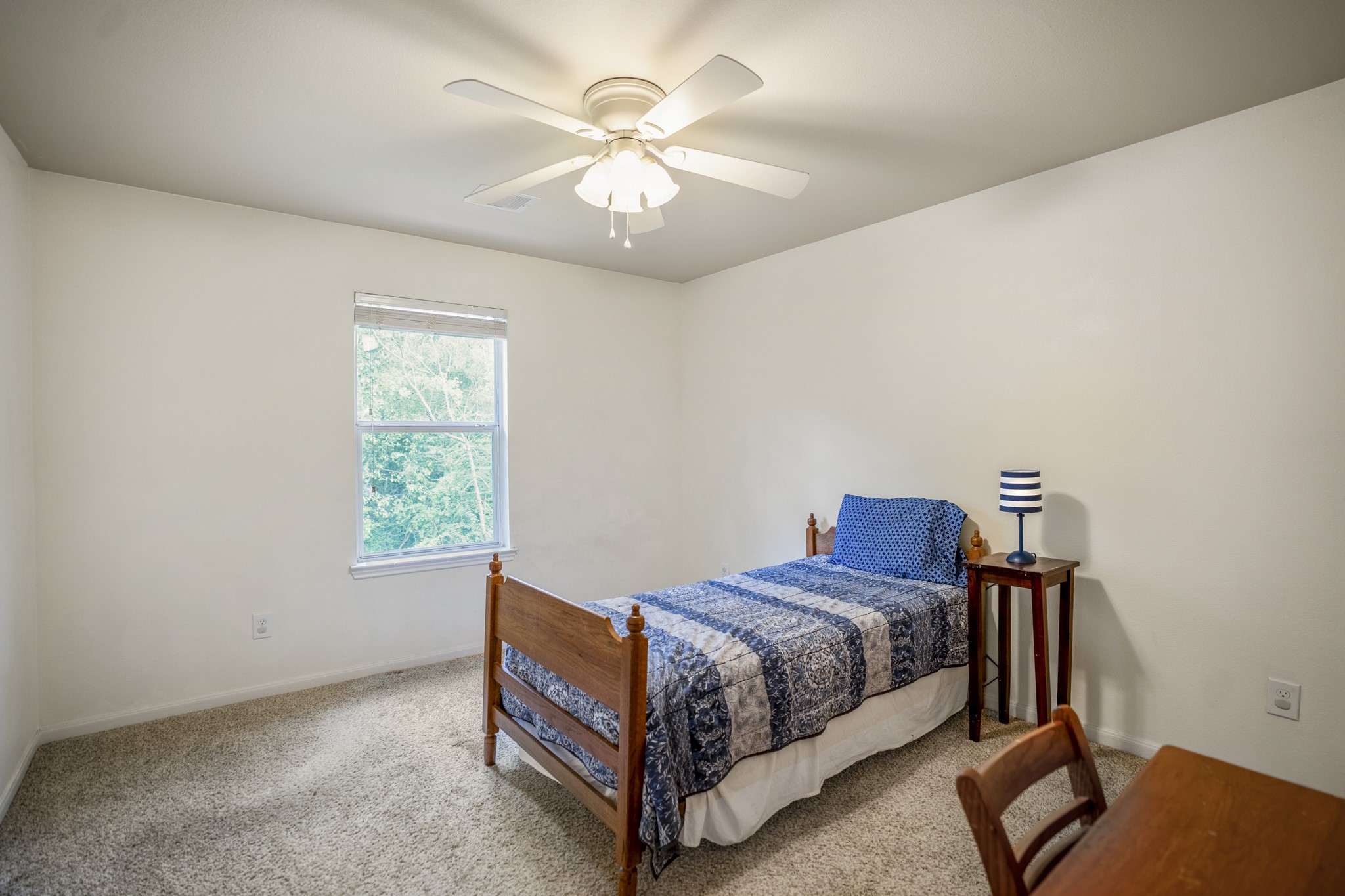 The fourth bedroom continues the upstairs flow with new carpet, neutral walls, a ceiling fan, and a window bringing in natural light.