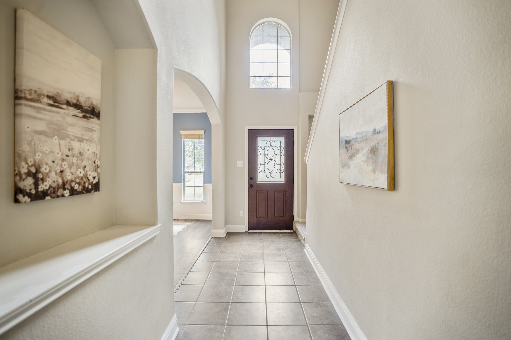 Back at the foyer, the staircase sits just to the left as you head toward the second floor. An art niche with a display shelf adds a little architectural detail along the wall, while the tall entry window and front door keep this part of the home bright and welcoming.