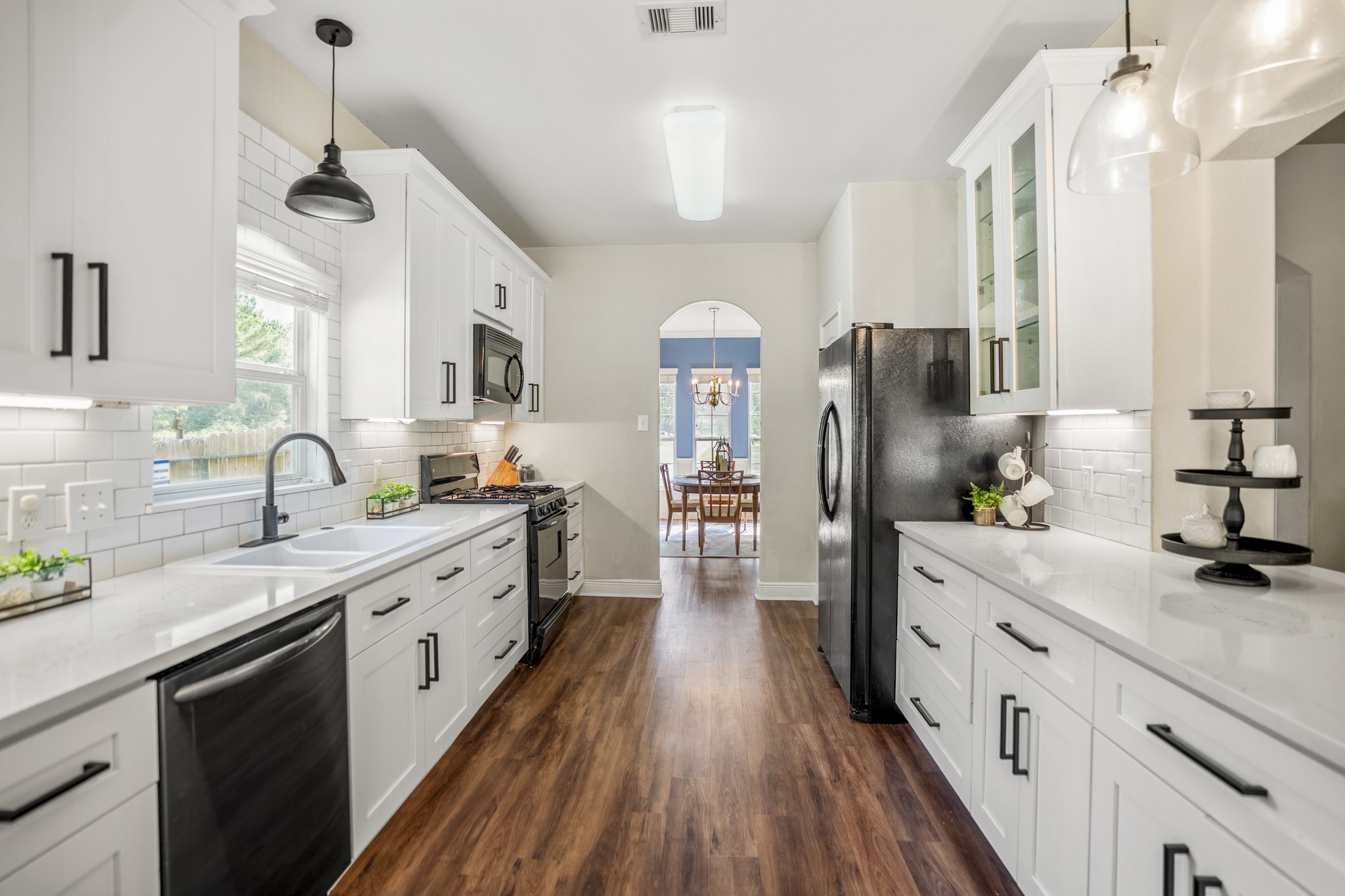 Step into the remodeled kitchen, where white cabinetry, black hardware, quartz countertops, subway tile backsplash, and modern pendant lighting give the space a fresh, cohesive look. The breakfast bar was reworked as part of the remodel, opening the kitchen up for casual seating and serving, while deep drawers offer convenient storage for pots and pans. Under-cabinet lighting adds another layer of function, and the pantry door on the left keeps everyday staples close at hand.