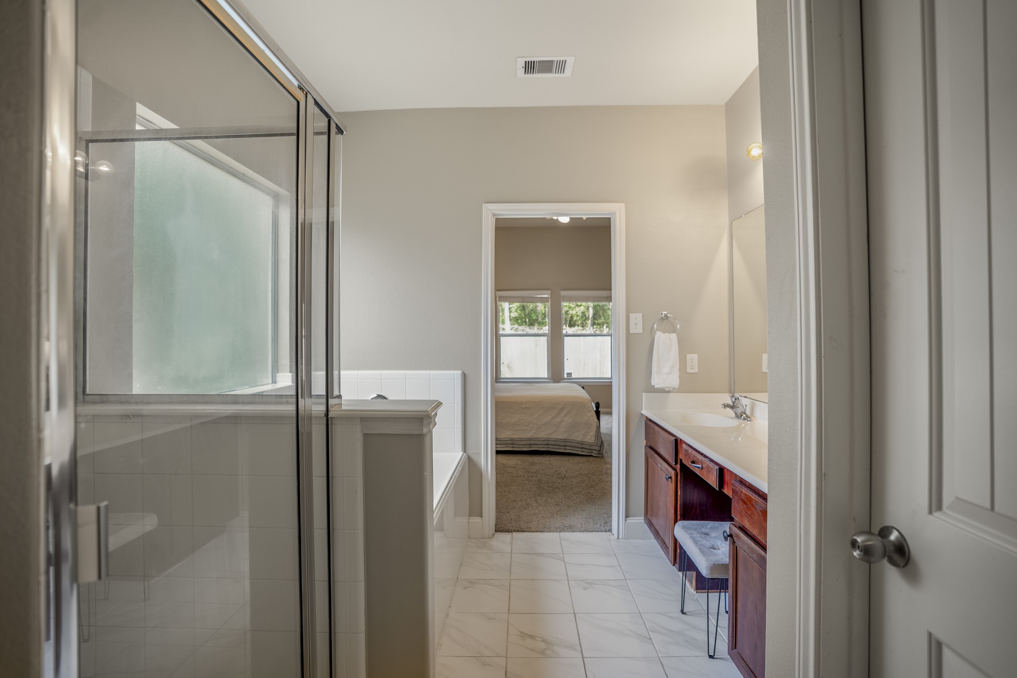Looking back through the primary bath, the shower sits to the left with the dual vanity running along the opposite side. Straight ahead, the doorway leads back into the primary bedroom, making the whole suite feel connected and easy to move through from one space to the next.