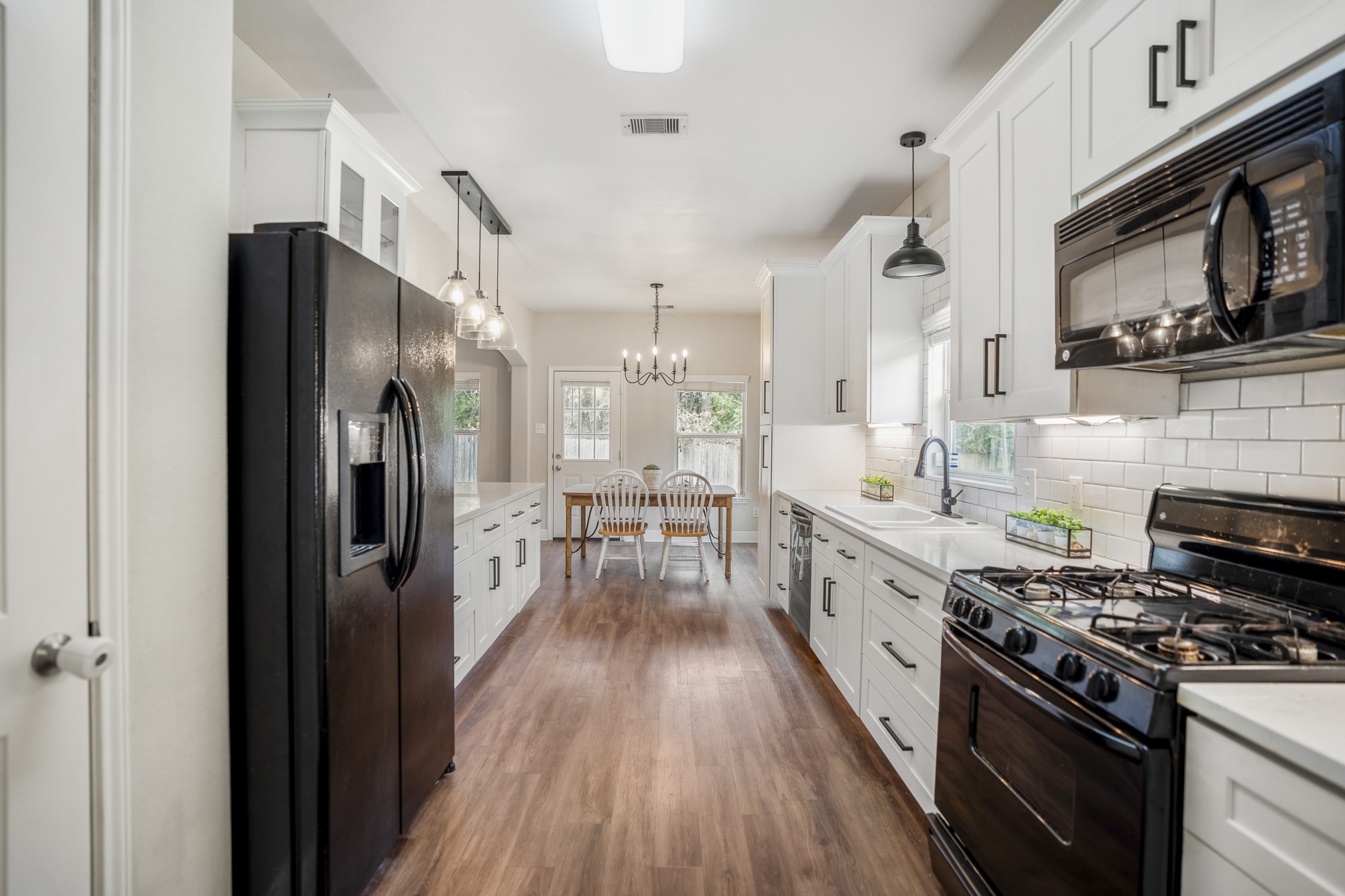 Looking back through the kitchen, the details really come into focus: quartz countertops, glass-front cabinetry, pendant lighting over the sink, a window above the double-basin sink, and a pull-down faucet make the workspace feel both practical and thoughtfully finished. Cabinetry and prep space run along both sides, while vinyl plank flooring carries you toward the formal dining room at the far end for an easy prep-to-table flow.