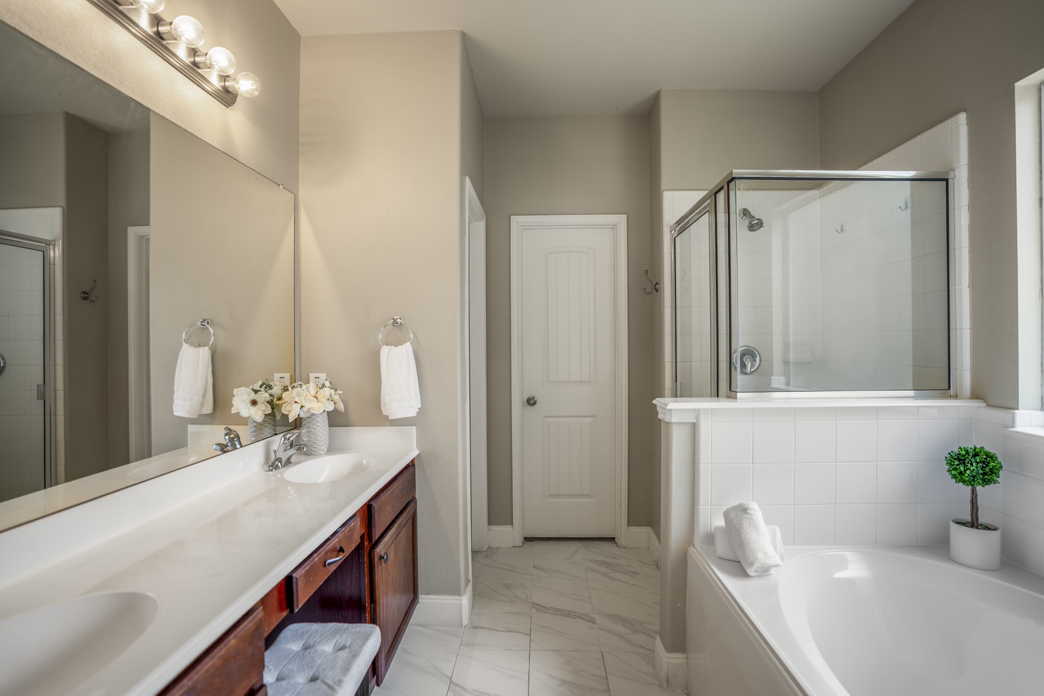 Step into the primary bath, where dual sinks are separated by extra counter space and a seated vanity area that makes the morning routine feel a little more functional. The soaking tub and separate shower line the opposite side, while new tile flooring runs throughout. Straight ahead, the door leads into the walk-in closet, while the doorway just to the left is the toilet.