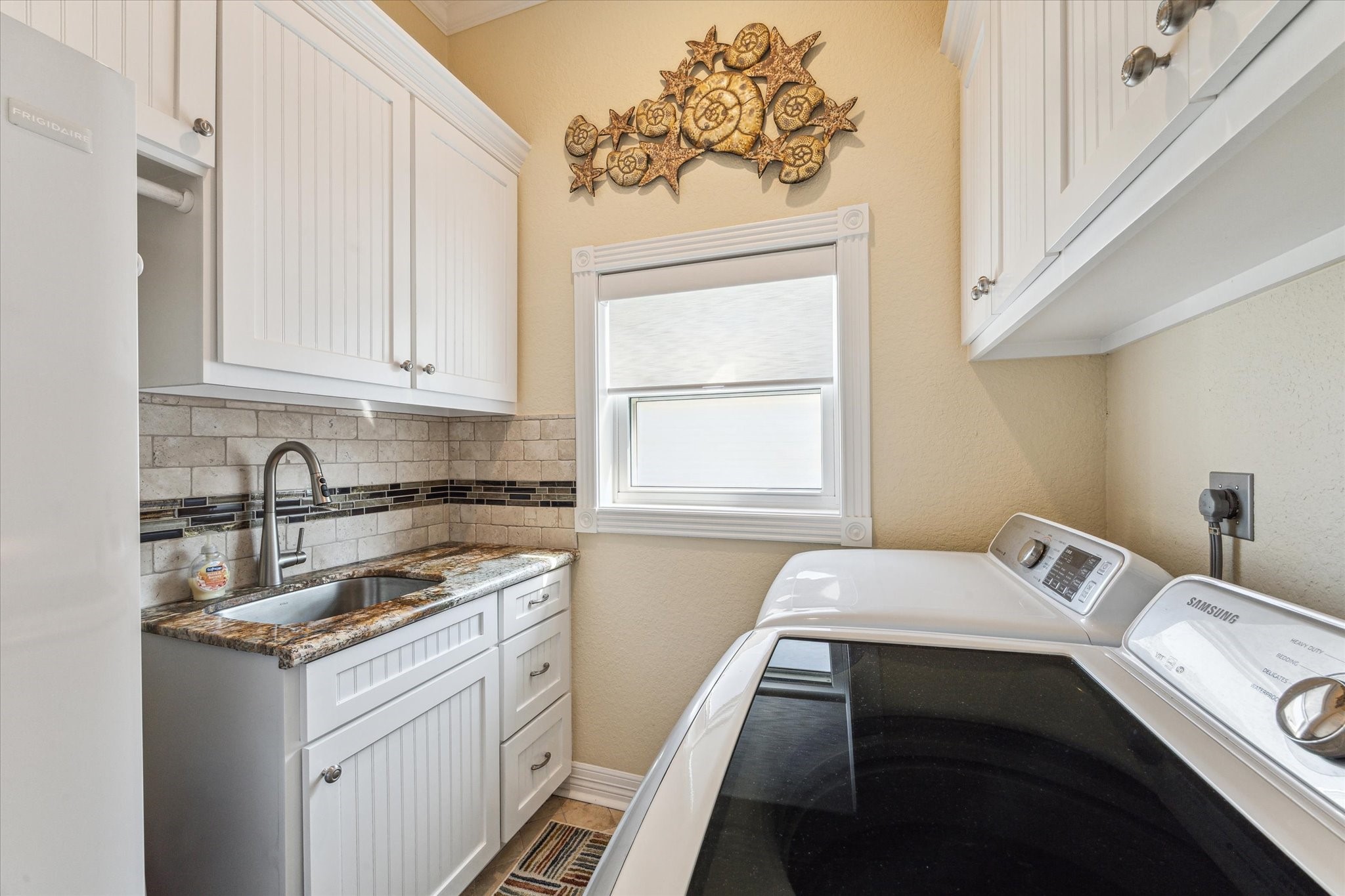 The laundry room was designed with ample  custom cabinetry, a sink with granite counters, and room for an additional refrigerator.
