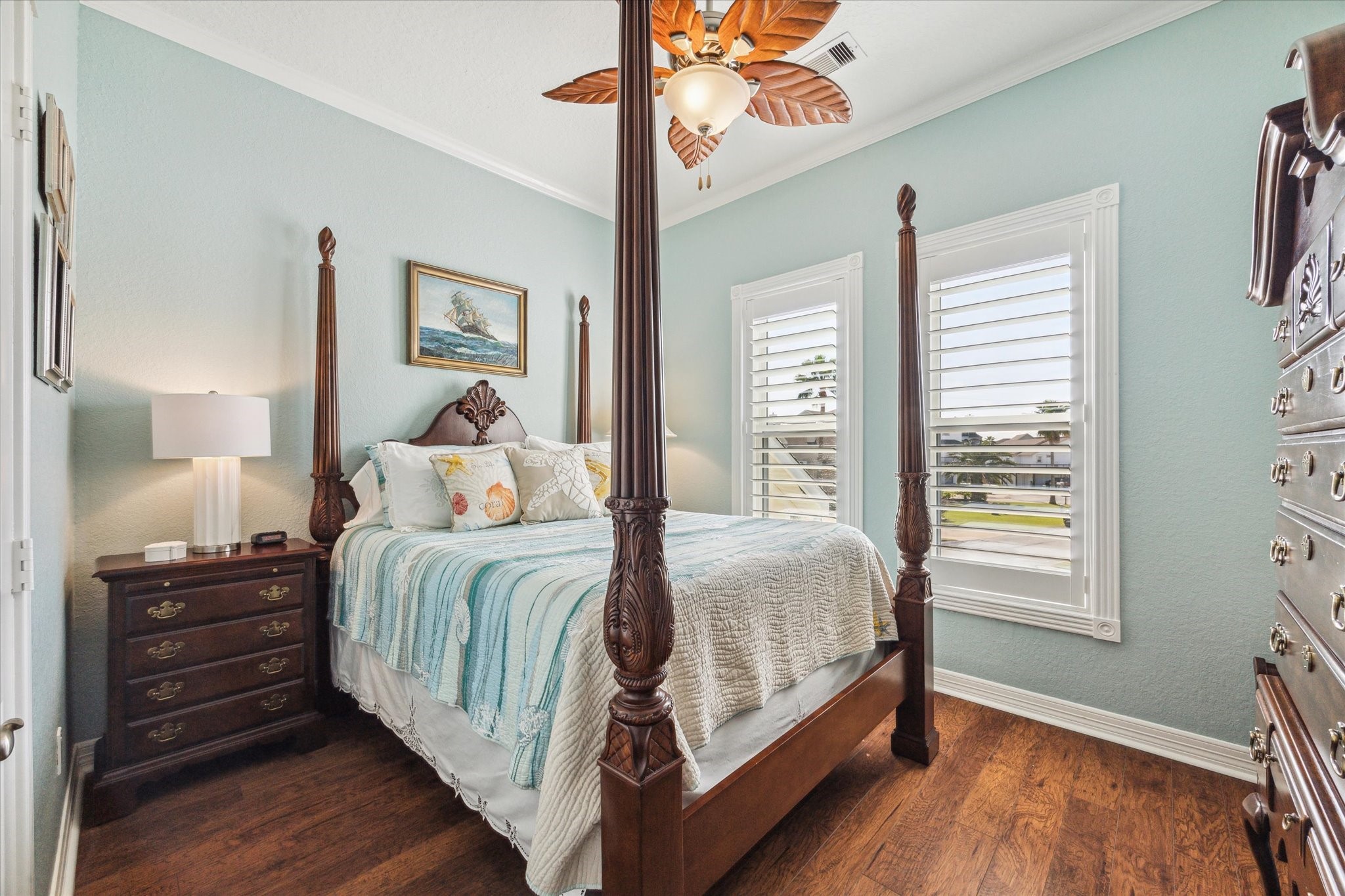 This bedroom provides a soothing paint color, wood floors and plantation shutters.