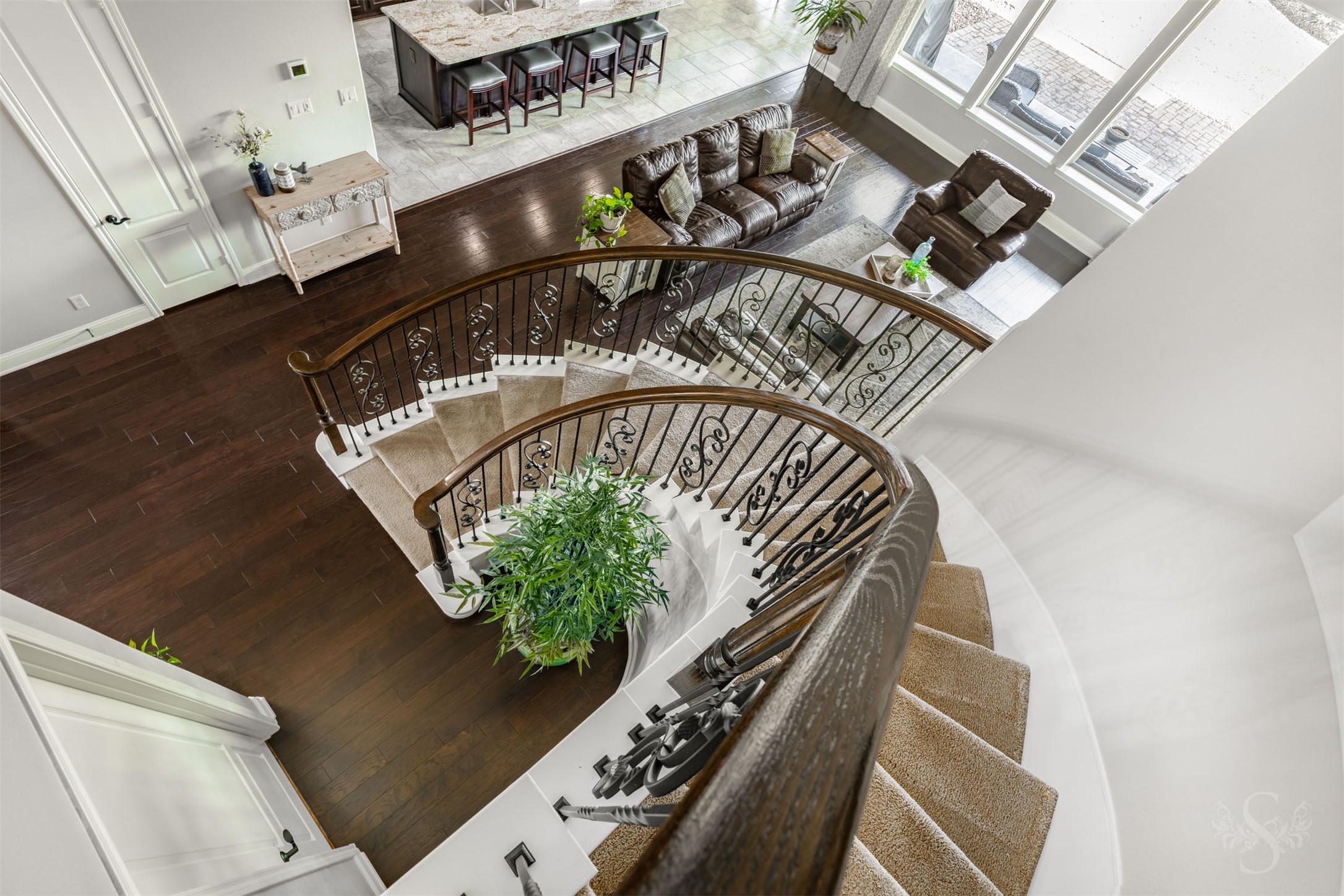 A spectacular view from above captures the sweeping curves of the staircase and the intricate ironwork that make it an architectural showpiece. Rich wood flooring, expansive windows and the open gathering spaces below reveal the homes stunning scale and beauty.