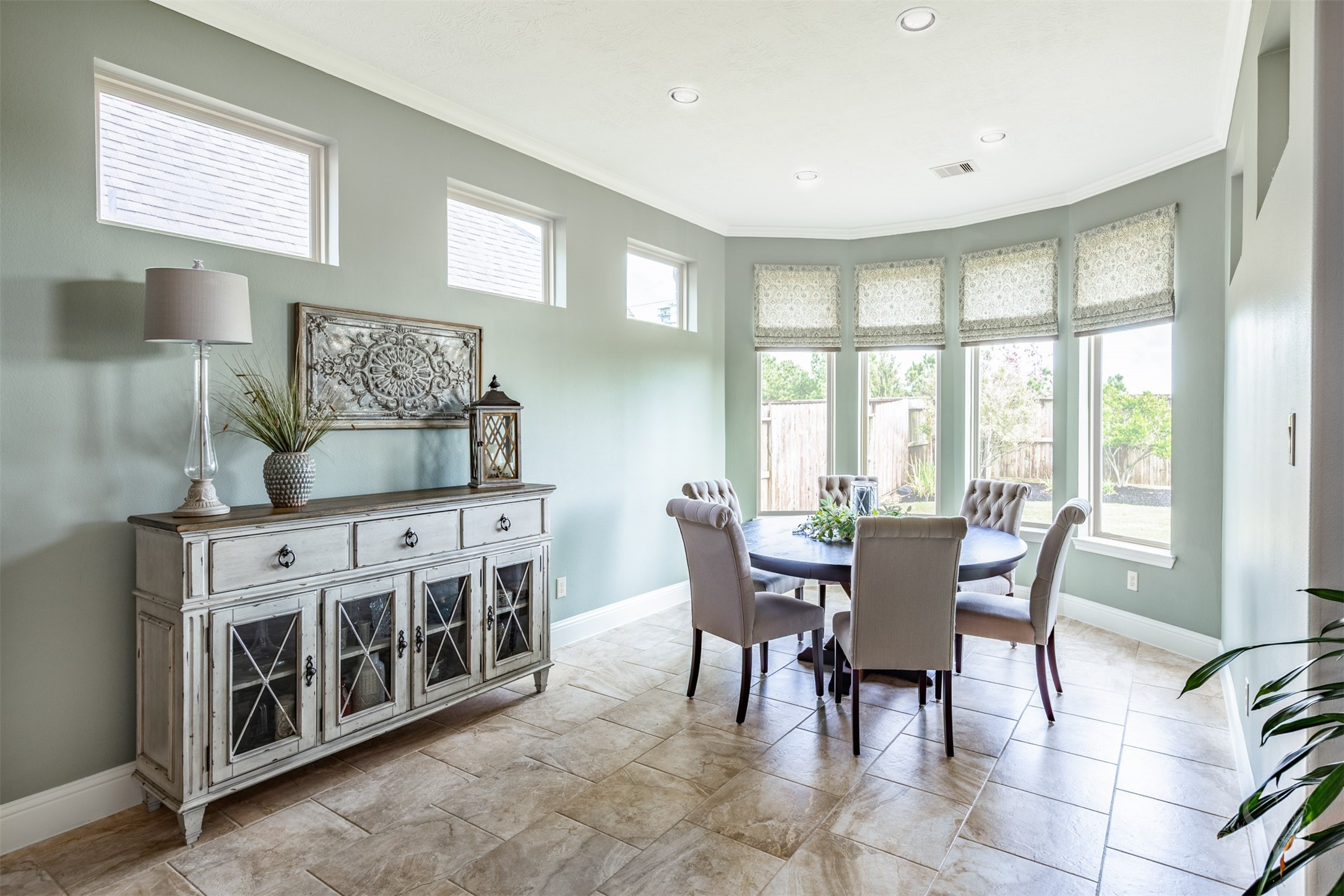 A beautiful bay of tall windows makes this bright and cheerful breakfast room a delightful place to start the day. Enjoy your morning coffee and breakfast with backyard views, surrounded by soft green walls, elegant crown molding and beautiful tile flooring.