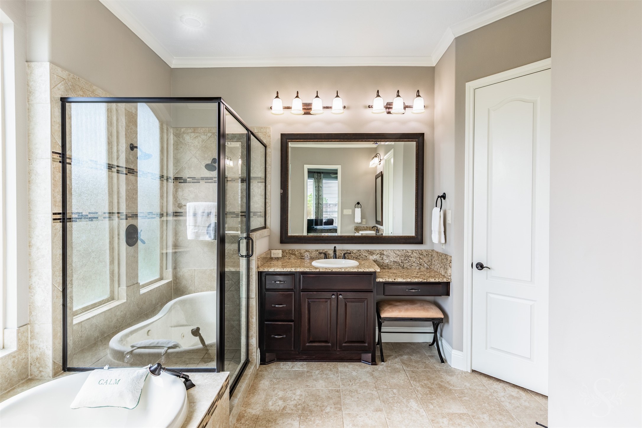 A granite-topped vanity with a seated dressing area offers a beautiful place to begin your day. The adjacent glass-enclosed shower features decorative tile accents that complement the baths warm finishes.
