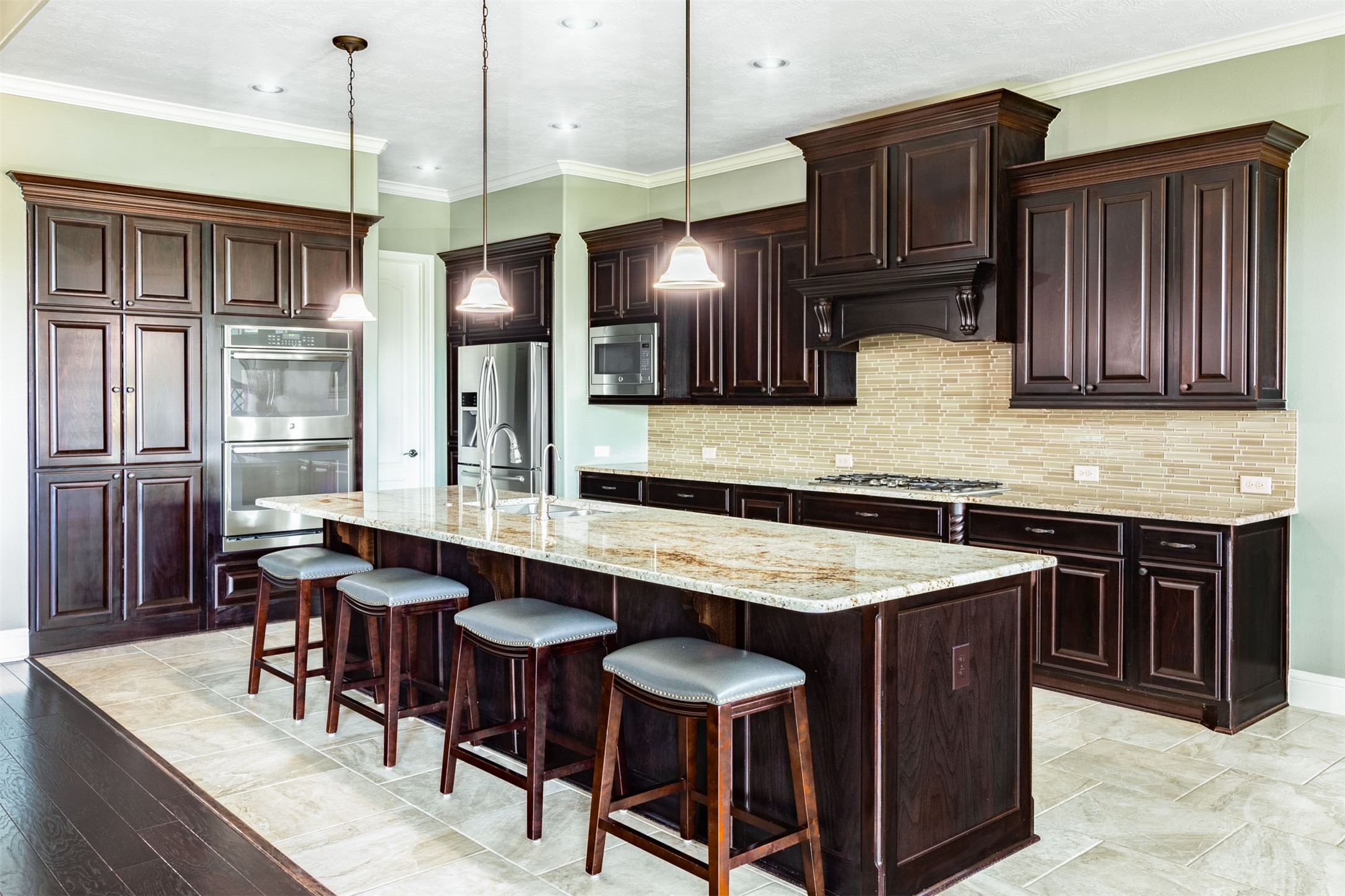 Beautiful raised-panel cabinetry with substantial crown detailing brings warmth and distinction to the spacious kitchen. Granite counters, a shimmering tile backsplash, stainless steel double ovens and a gas cooktop surround the oversized island, creating an inviting space for cooking and gathering.