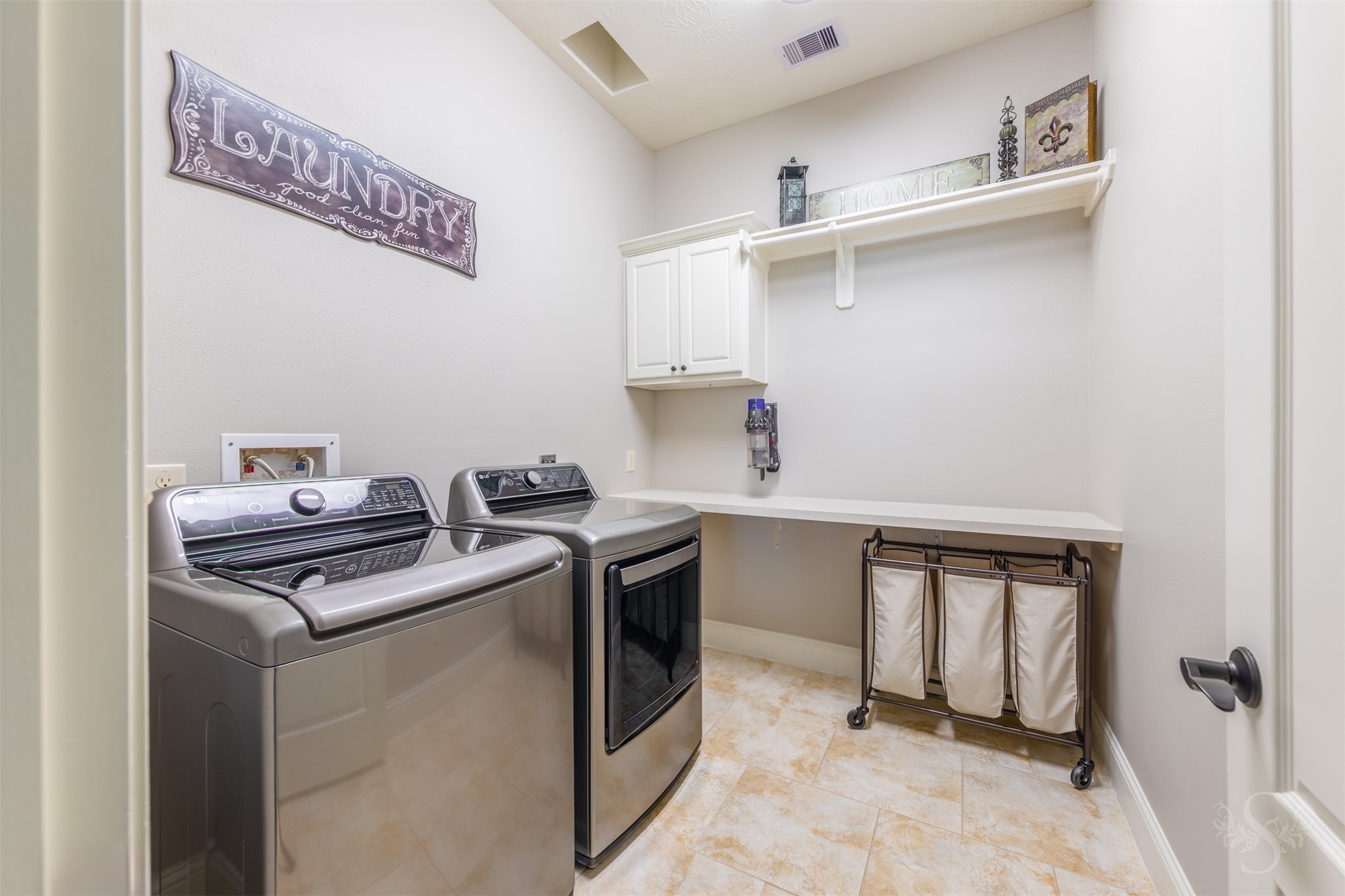 The spacious utility room features a long folding counter, white cabinetry and an overhead shelf with a hanging rod. Tile flooring and ample space for sorting laundry help keep daily routines organized.