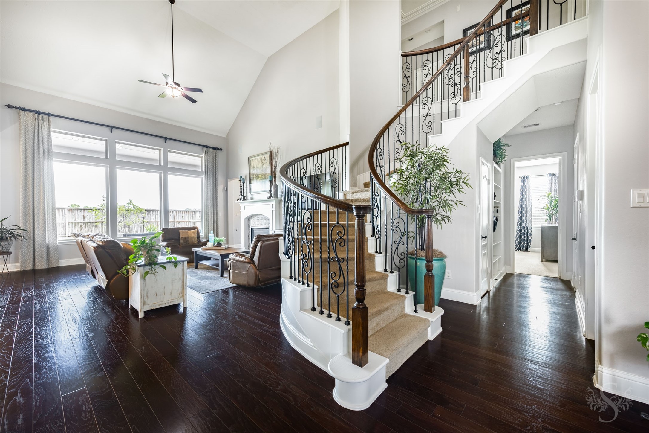 A sweeping curved staircase with decorative iron balusters and a rich wood handrail creates a stunning architectural centerpiece. Beautiful wood flooring leads into the family room, where expansive windows and a dramatic ceiling height enhance the open design. A sweeping curved staircase with decorative iron balusters and a rich wood handrail creates a stunning architectural centerpiece. Beautiful wood flooring leads into the family room, where expansive windows and a dramatic ceiling height enhance the open design.