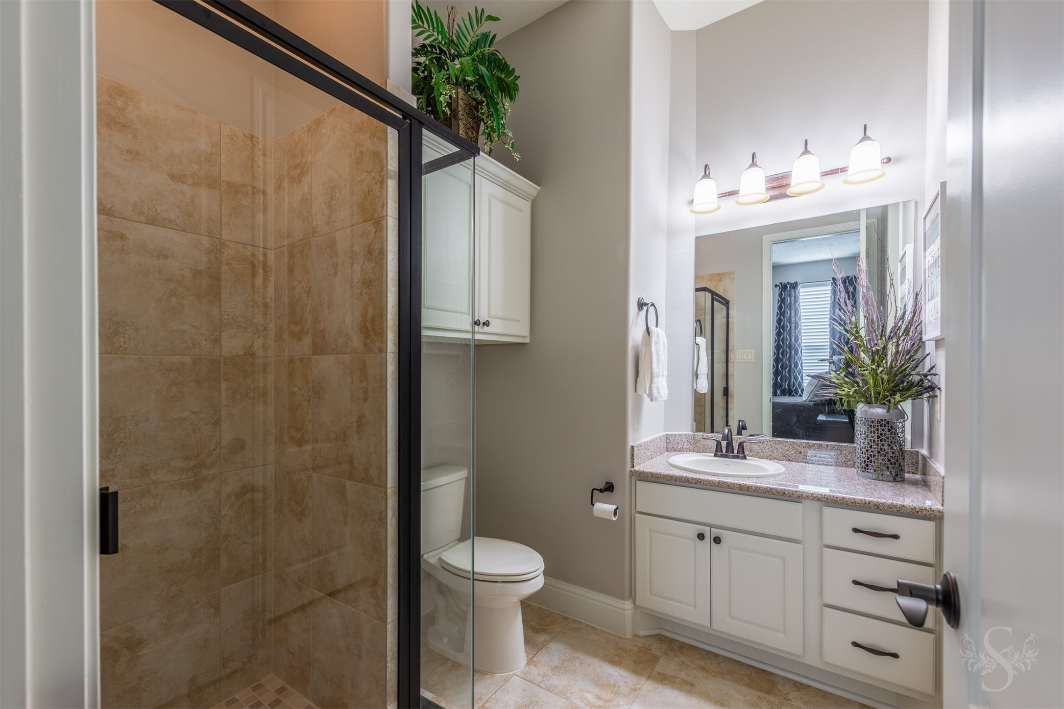 A crisp white vanity with a granite countertop and dark hardware gives this secondary bath an elegant, timeless look. A glass-enclosed tiled shower and additional wall cabinetry provide everyday comfort and convenient storage.