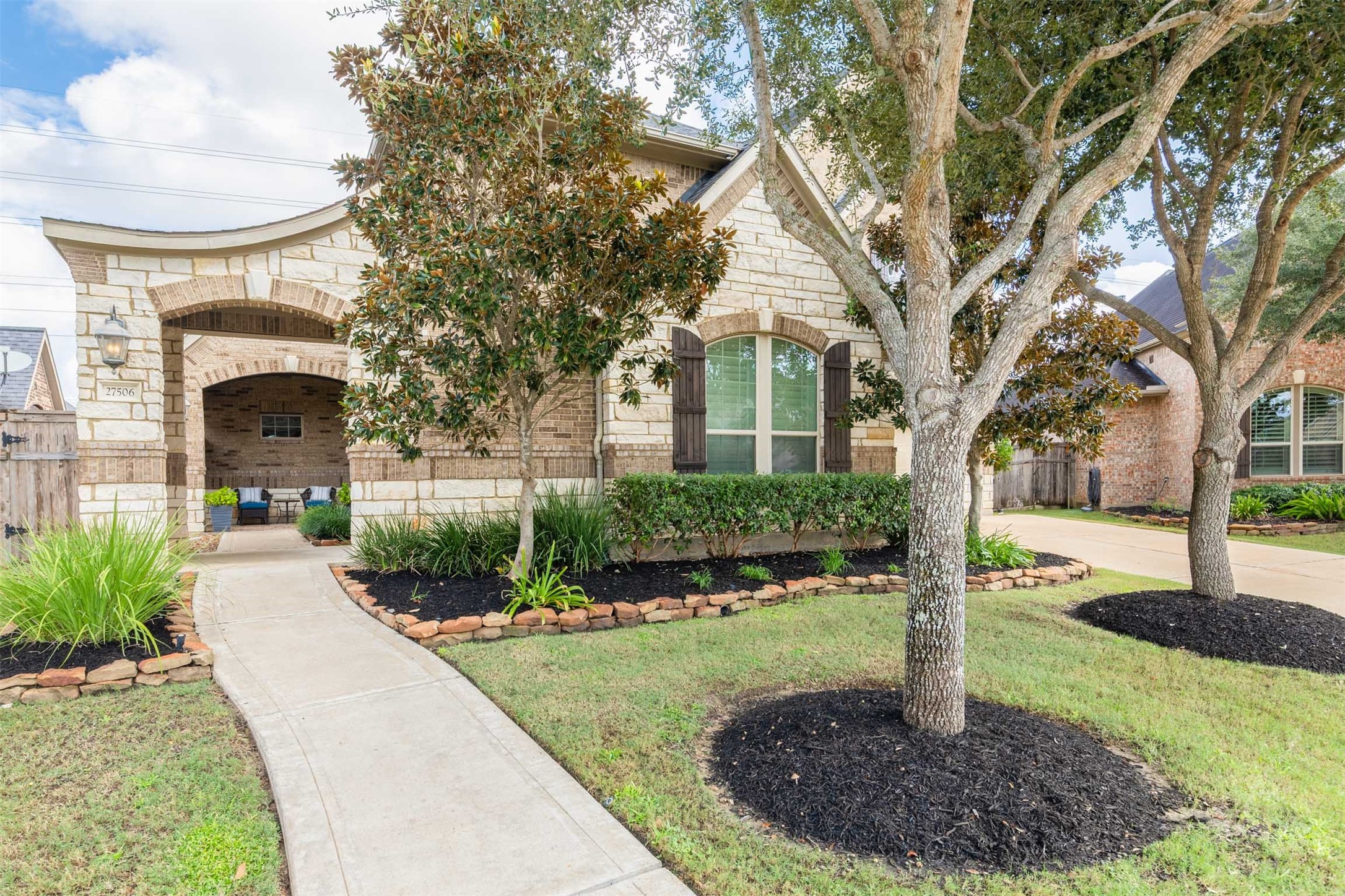 A gently curved walkway leads past mature trees and beautifully landscaped beds to the striking arched courtyard entrance. The elegant blend of brick and stone creates a memorable welcome before you step inside.