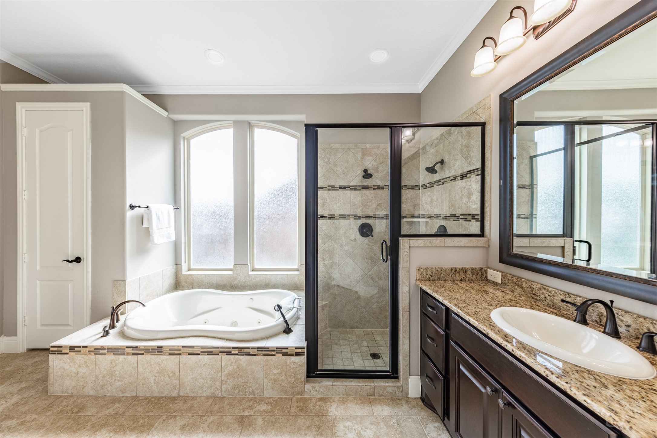 Relax in the jetted tub beneath gracefully arched privacy windows, surrounded by warm tile and mosaic detailing. A separate shower with dual showerheads and a generous granite-topped vanity complete this luxurious retreat.