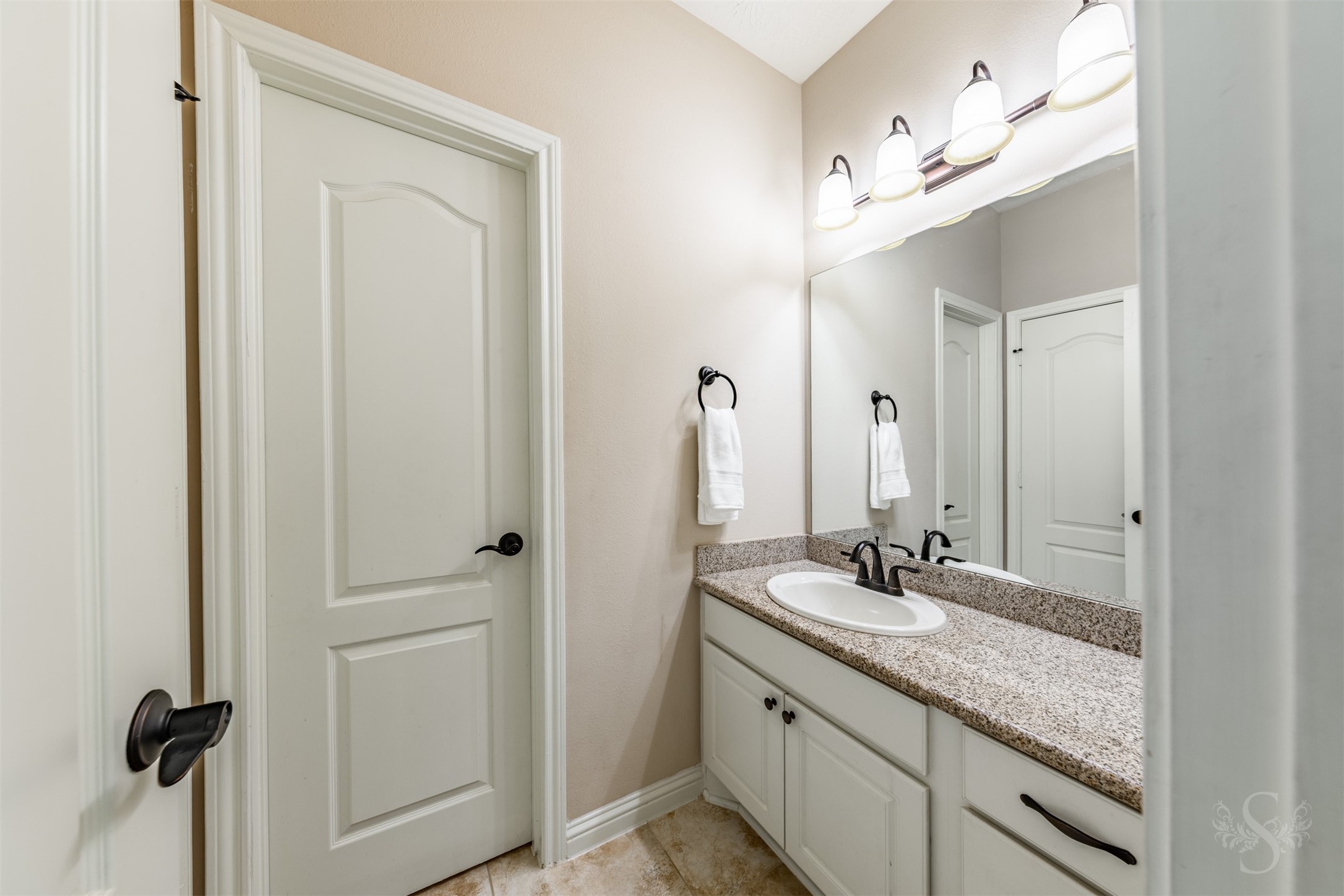 White cabinetry and a polished granite countertop bring timeless appeal to this upstairs vanity area. A large mirror, elegant lighting and dark hardware complete the space with style and everyday convenience.