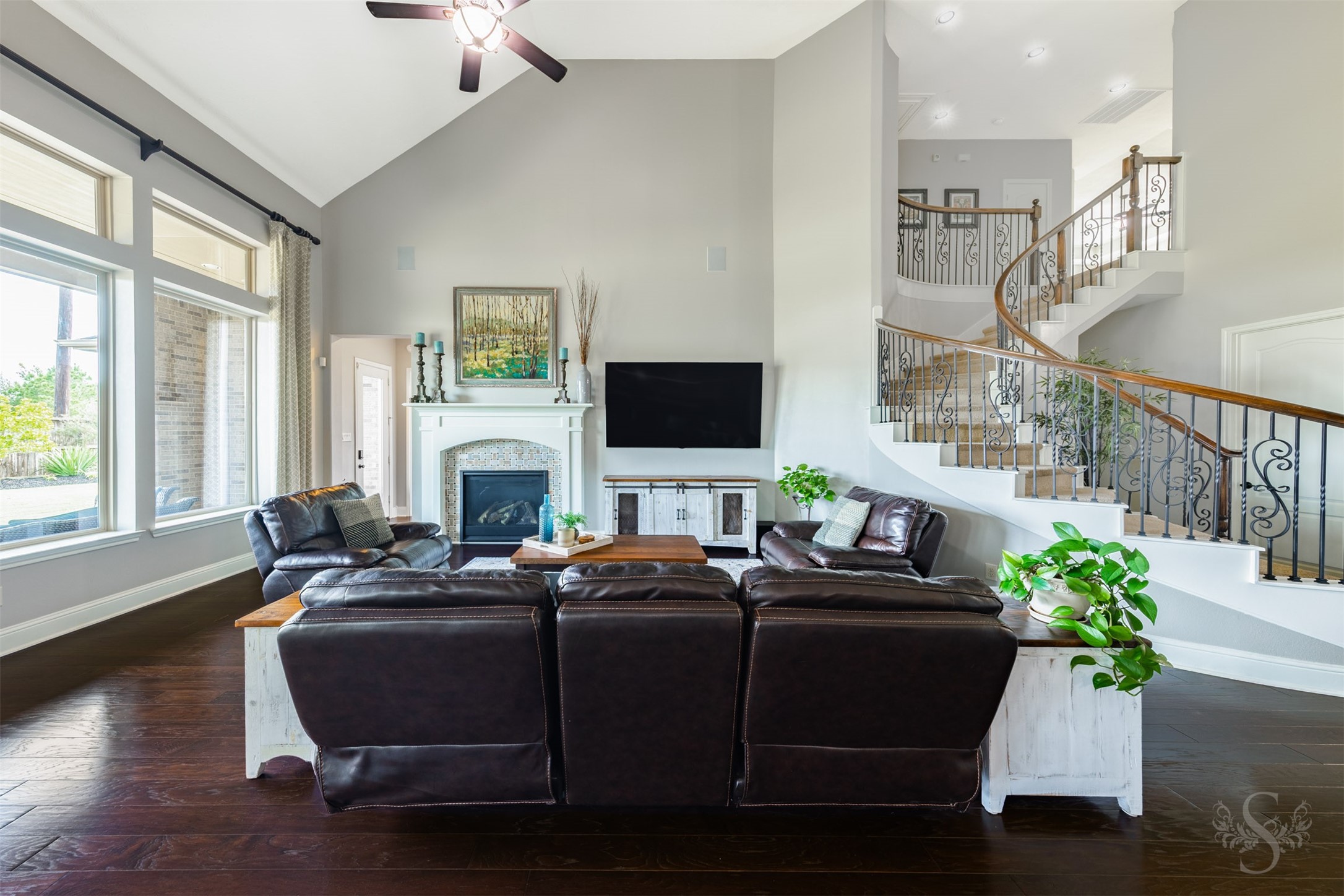 A wall of windows with transoms above fills the spacious family room with backyard views. The fireplaces mosaic tile surround and classic white mantel provide a beautiful focal point, complemented by the sweeping staircase and intricate ironwork. A wall of windows with transoms above fills the spacious family room with backyard views. The fireplaces mosaic tile surround and classic white mantel provide a beautiful focal point, complemented by the sweeping staircase and intricate ironwork.