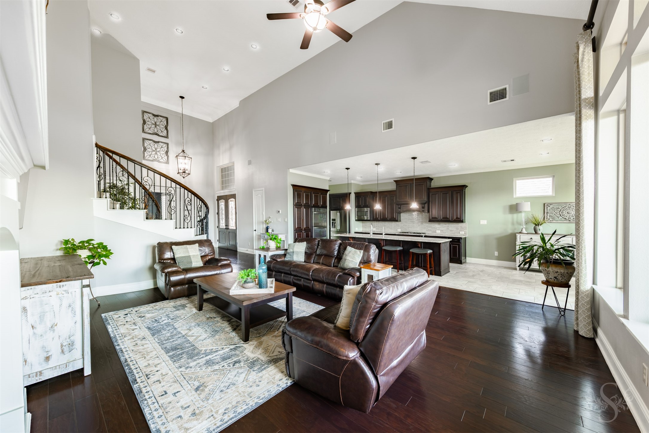 The open concept floor plan showcases a stunning family room with a vaulted ceiling, rich wood flooring and expansive windows. An oversized kitchen island overlooks the gathering space, keeping everyone connected while preparing meals or entertaining friends. The open concept floor plan showcases a stunning family room with a vaulted ceiling, rich wood flooring and expansive windows. An oversized kitchen island overlooks the gathering space, keeping everyone connected while preparing meals or entertaining friends.