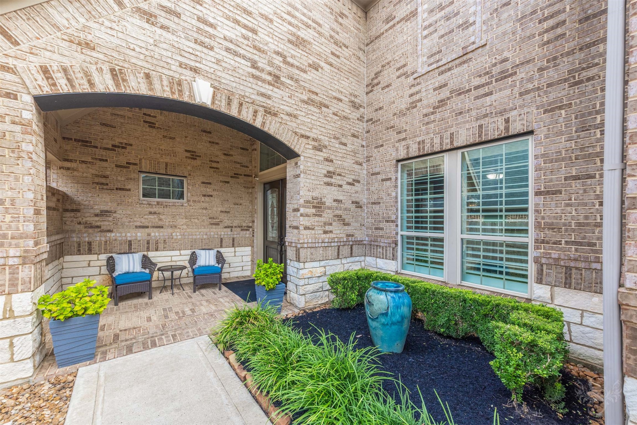 Tucked beneath a graceful brick arch, the sheltered front porch offers an inviting spot for morning coffee or quiet conversation. Brick paving, stone detailing and manicured greenery give this charming courtyard timeless appeal.