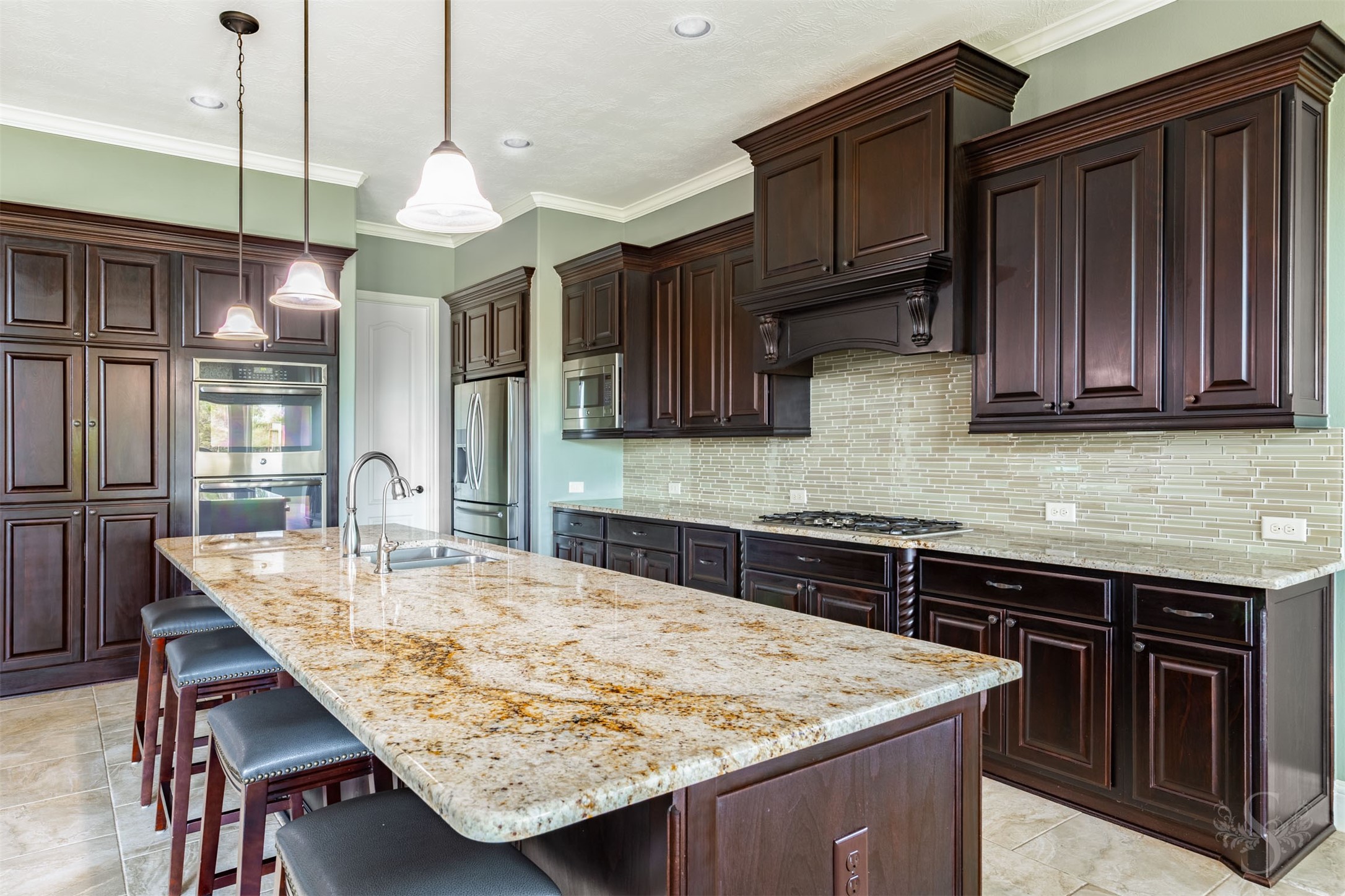 Gorgeous granite stretches across the oversized island, offering abundant workspace and seating for casual meals or conversation with the cook. A gas cooktop, decorative wood vent hood, stainless steel double ovens and extensive cabinetry complete this impressive culinary space.