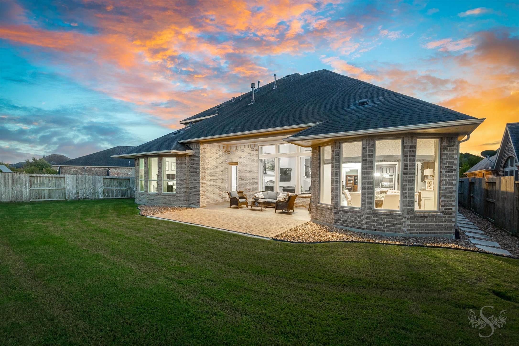Beautiful bay windows flank the inviting covered patio, creating a striking backdrop for outdoor living. An extended paver patio overlooks the spacious fenced backyard, offering plenty of space for gathering with friends and enjoying time outdoors.