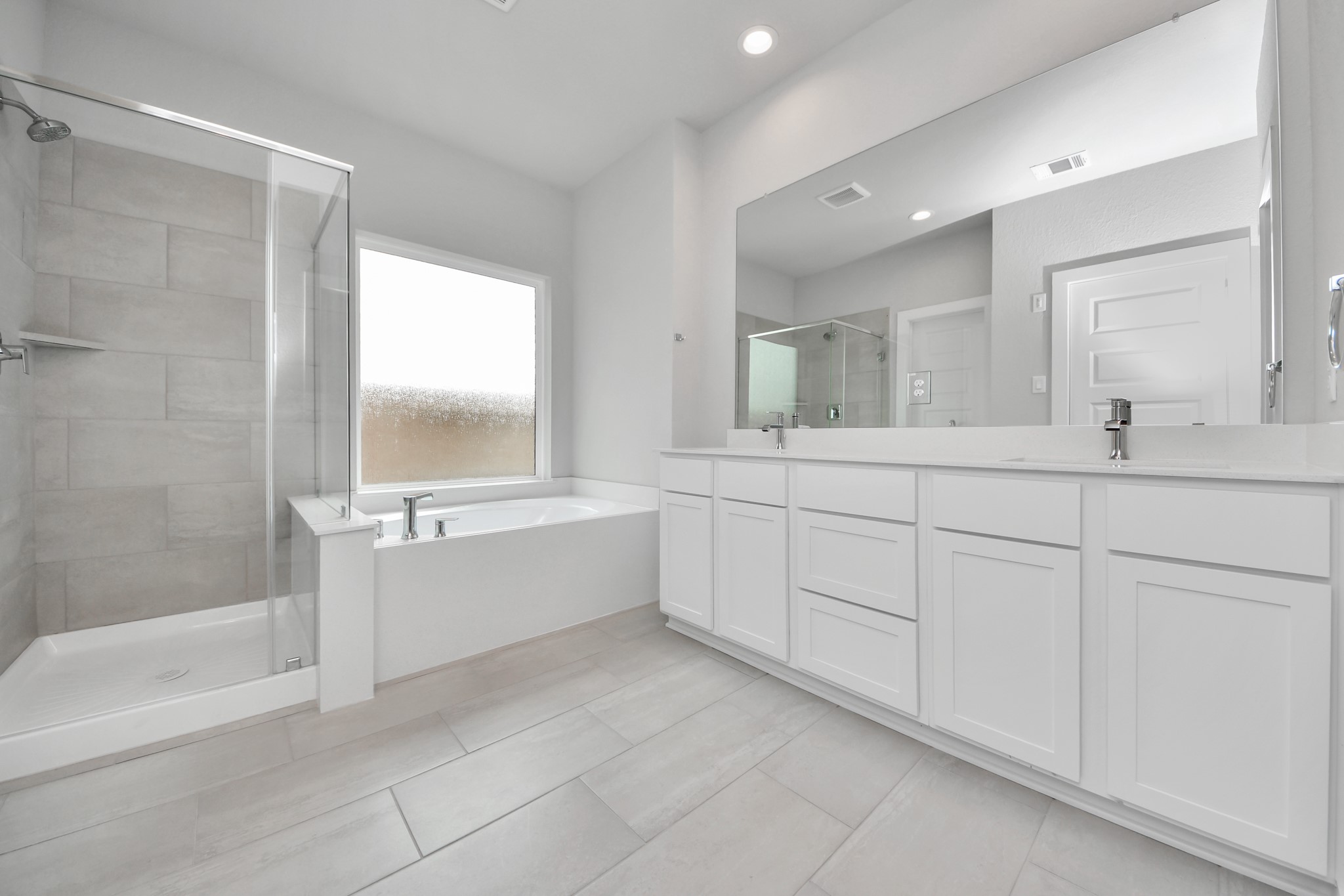 Escape to a spa-like oasis in this primary bathroom. Enjoy a walk-in shower with tile surround, a separate garden tub with custom detailing, and an elegant vanity featuring light countertops, modern hardware, and beautiful vanity lights. Experience luxury and relaxation in every detail. Sample photo of completed home with similar floor plan. Actual colors and selections may vary.