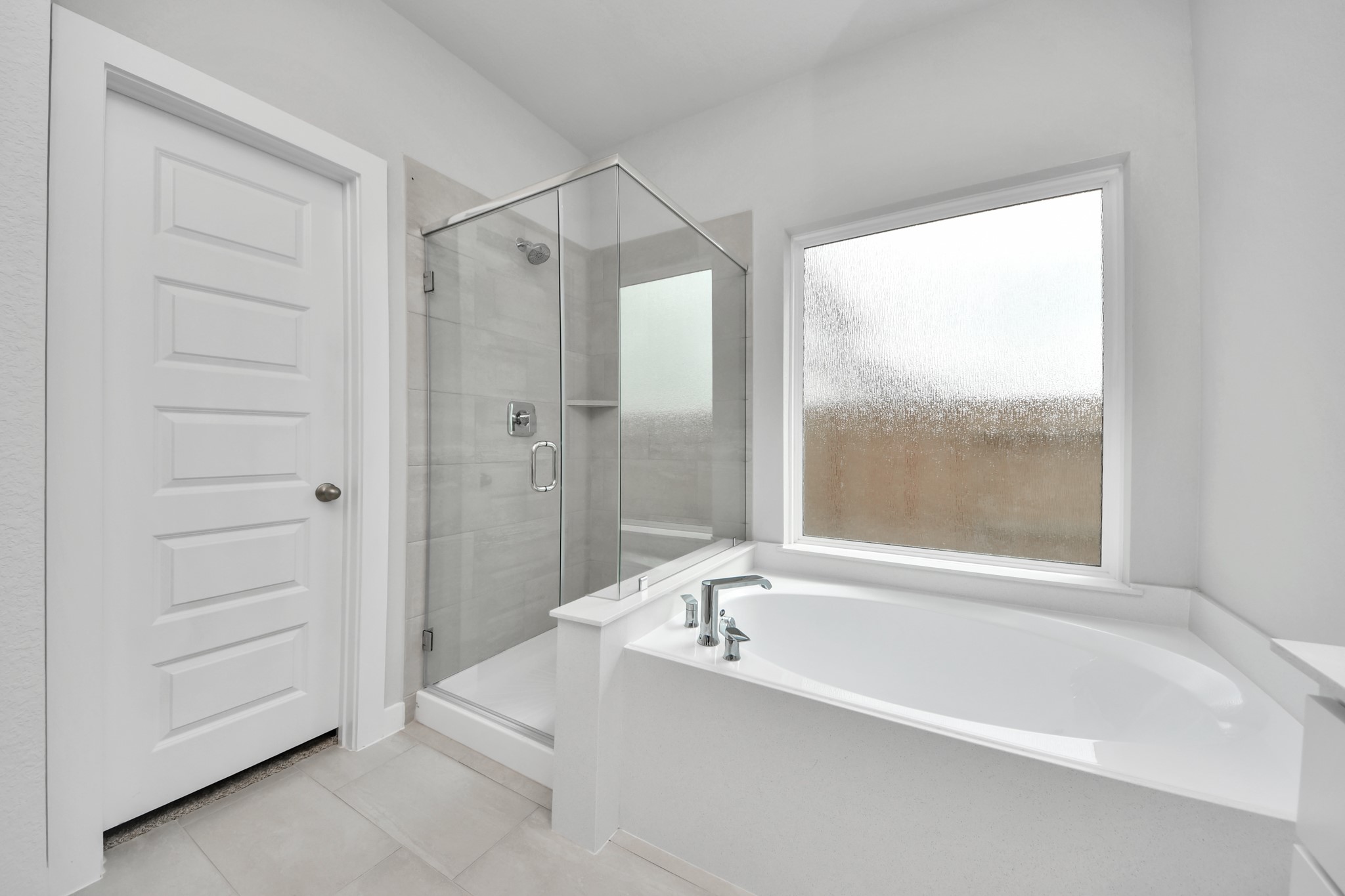 Indulge in a spa-like retreat within the confines of this primary bathroom. Delight in a spacious walk-in shower enveloped in stylish tile surround, unwind in a separate garden tub adorned with custom detailing. Sample photo of completed home with similar floor plan. Actual colors and selections may vary.