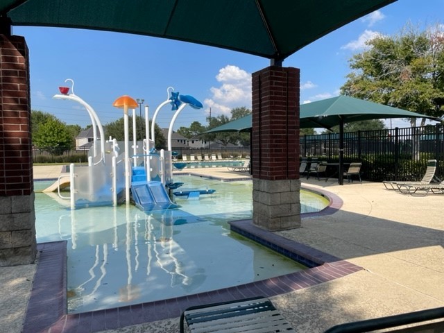 Charming community pool area featuring a fun children's splash zone with slides and water features, surrounded by shaded seating for relaxation.