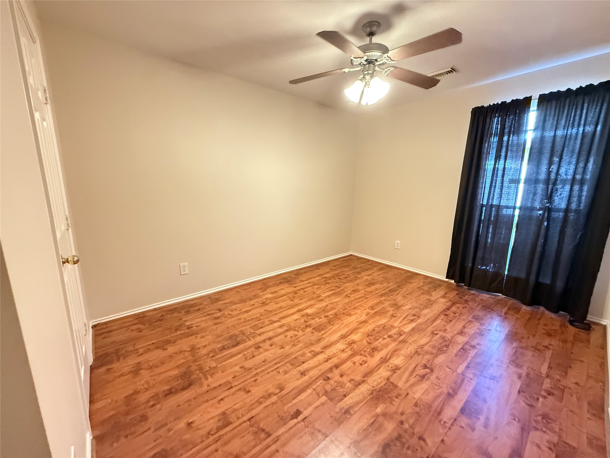 Guest bedroom 3 featuring warm vinyl plank  floors, a ceiling fan, and ample natural light through large windows with dark curtains.