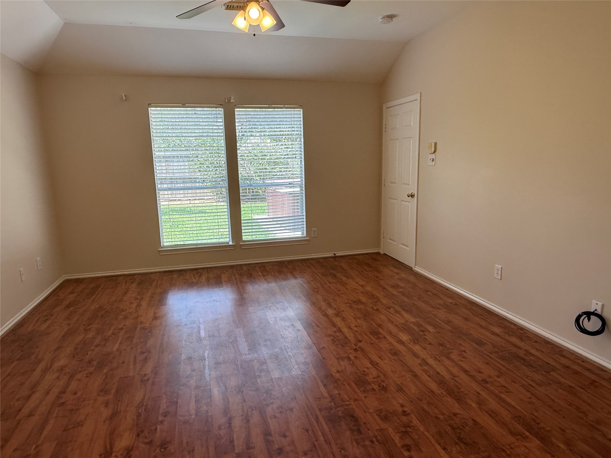 Primary bedroom with rich luxury vinyl plank flooring, large windows for natural light, and a ceiling fan for comfort.