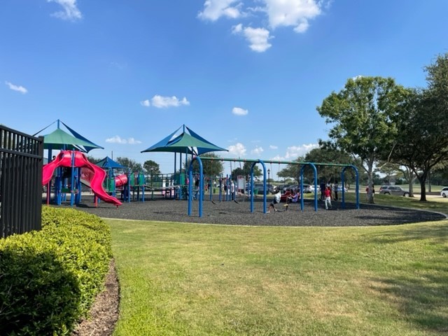 Charming community playground featuring vibrant play structures, surrounded by lush green lawns and shady trees, perfect for family fun and outdoor activities.
