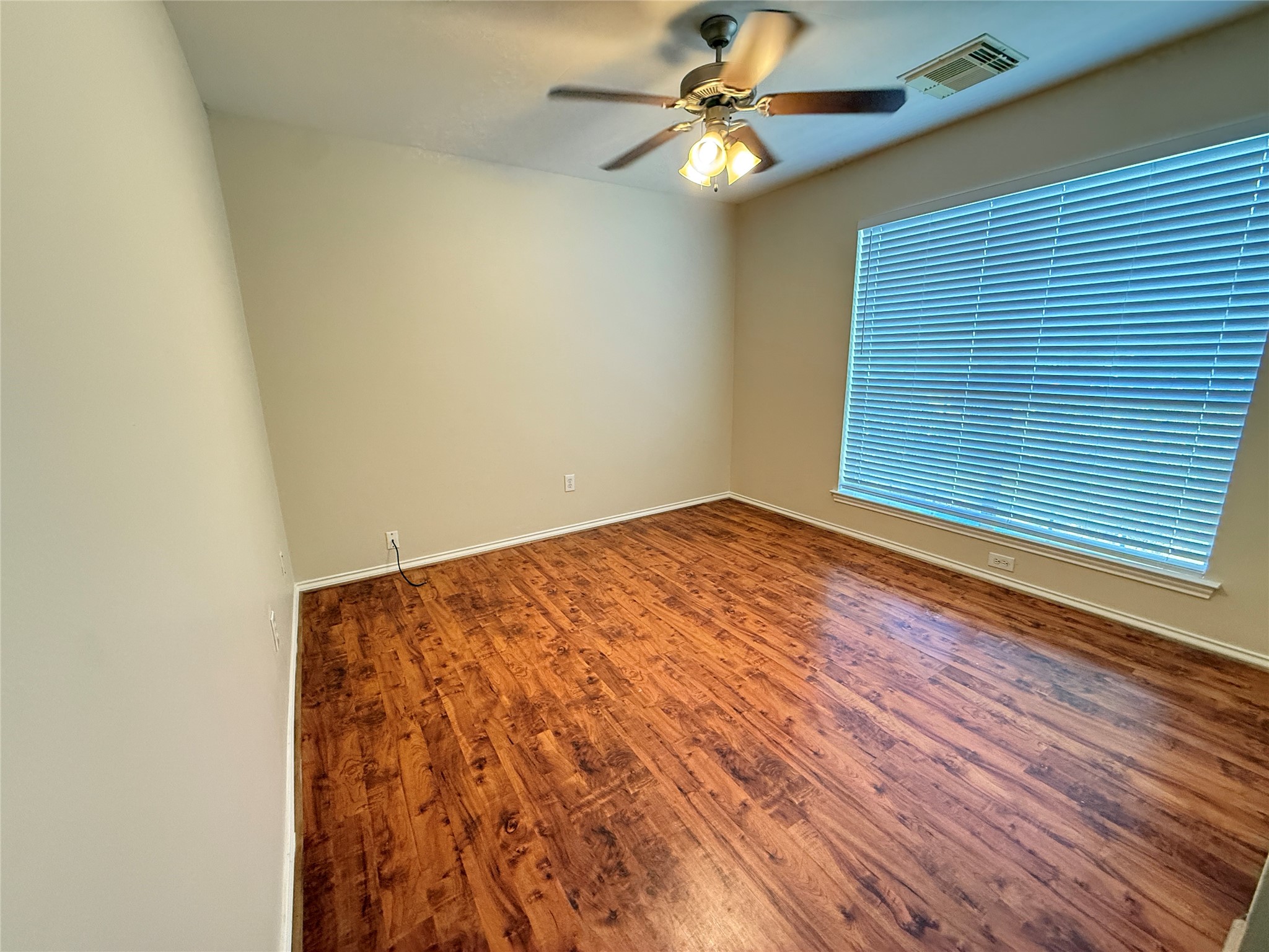 Second bedroom featuring rich vinyl plank floors, a large window with blinds for ample natural light, and a ceiling fan for comfort.
