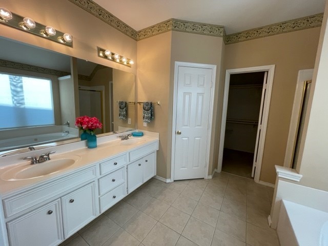 Spacious bathroom featuring a double vanity with ample storage, elegant lighting, and a walk-in closet.