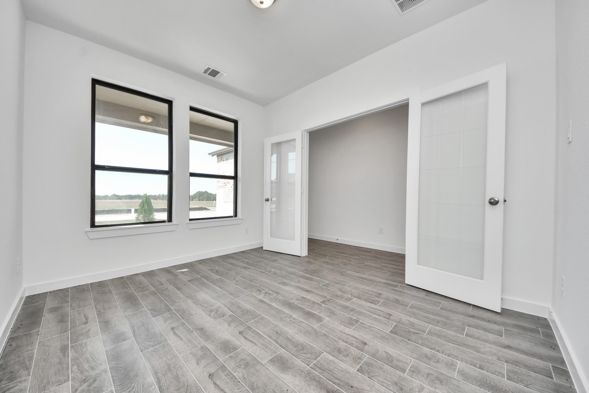 Experience the perfect blend of sophistication and warmth in this home office, boasting elegant wood-look tile flooring and flooded with natural light from expansive windows and French doors. Sample photo of completed home with similar floor plan. Actual colors and selections may vary.