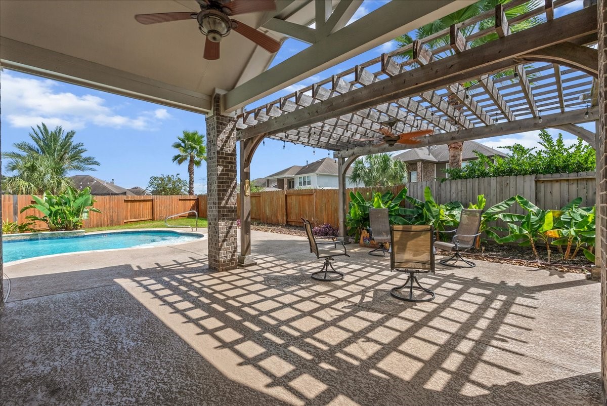 Imagine your family enjoying outdoor living with a spacious patio featuring a pergola, ceiling fan, and stylish seating area, overlooking a sparkling pool surrounded by lush greenery.