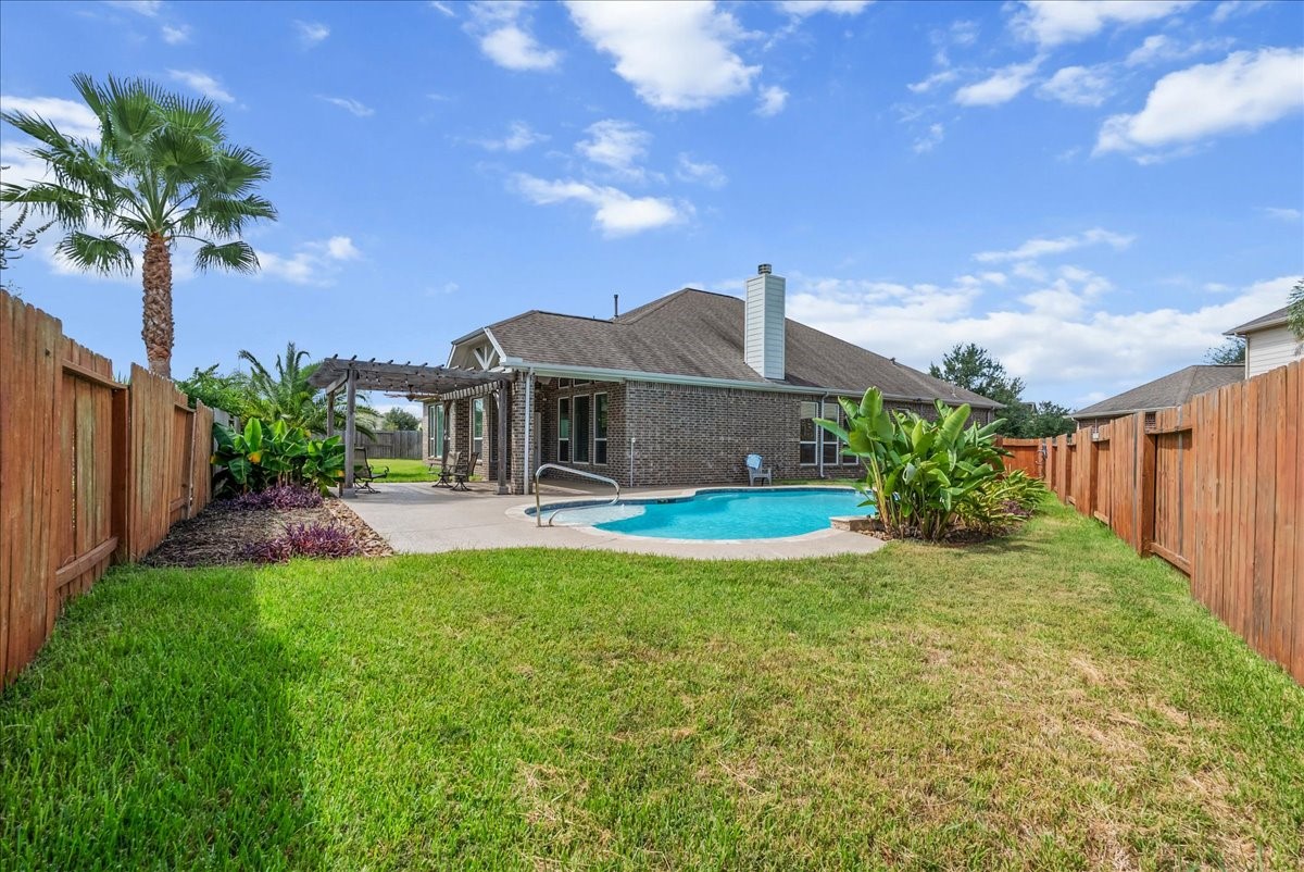 Relax in a spacious backyard featuring a sparkling pool, lush greenery, and a charming pergola, all enclosed by a wooden fence for privacy.