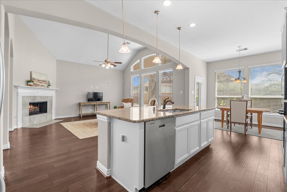 Spacious open-concept living area featuring a modern kitchen with granite countertops, an inviting dining space, and a cozy living room with a fireplace, all enhanced by abundant natural light from large windows.