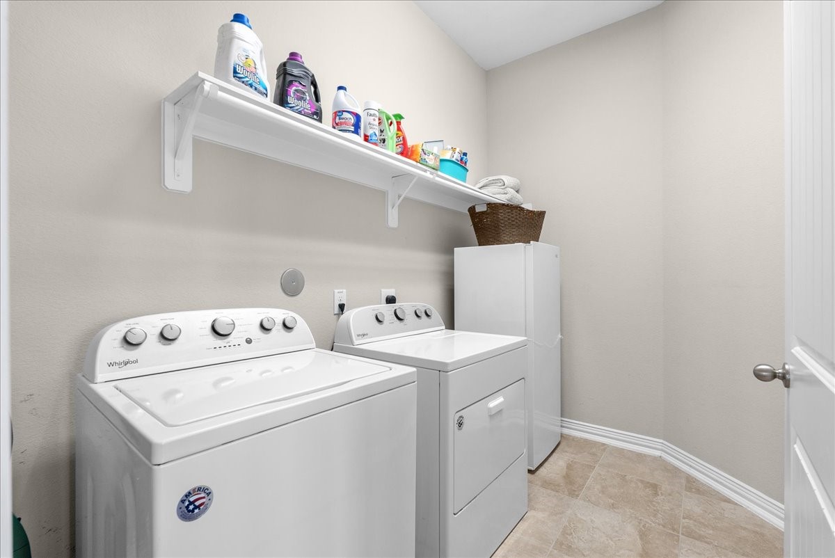 Spacious laundry room located inside the house equipped with washer and dryer, ample shelving for organization, and neutral tile floors for easy maintenance.