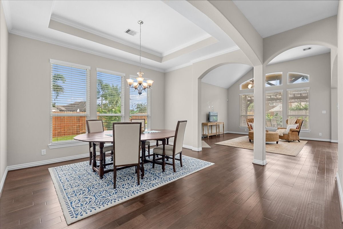 Elegant open-plan dining and living area featuring high ceilings, rich engineered hardwood floors, and abundant natural light from large windows overlooking the backyard. Elegant open-plan dining and living area featuring high ceilings, rich engineered hardwood floors, and abundant natural light from large windows overlooking the backyard.