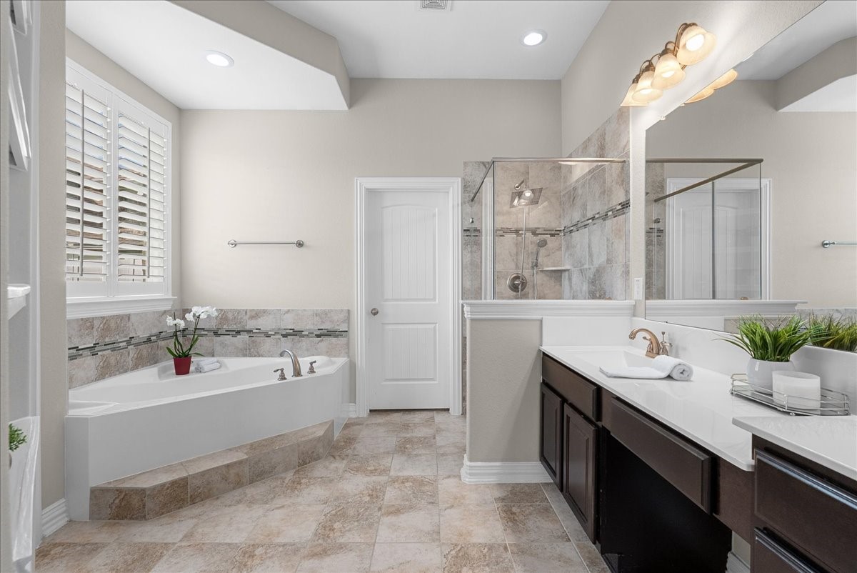 Come enjoy this luxurious bathroom featuring a spacious soaking tub, elegant dual vanities, and a sleek glass-enclosed shower, all accentuated by soft, neutral tones and ample natural light.