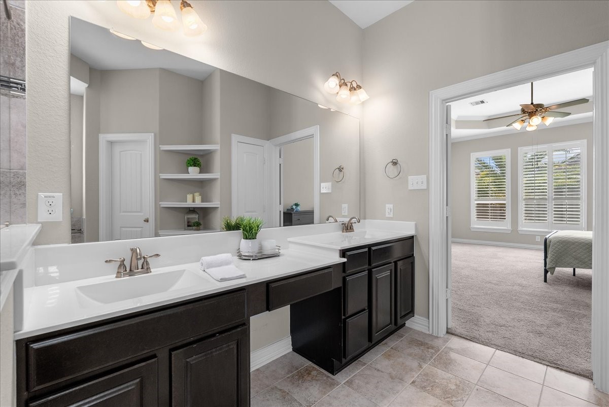 Spacious bathroom with dual sinks, elegant fixtures, and ample storage, seamlessly connecting to a bright bedroom featuring large windows that overlook the backyard area.